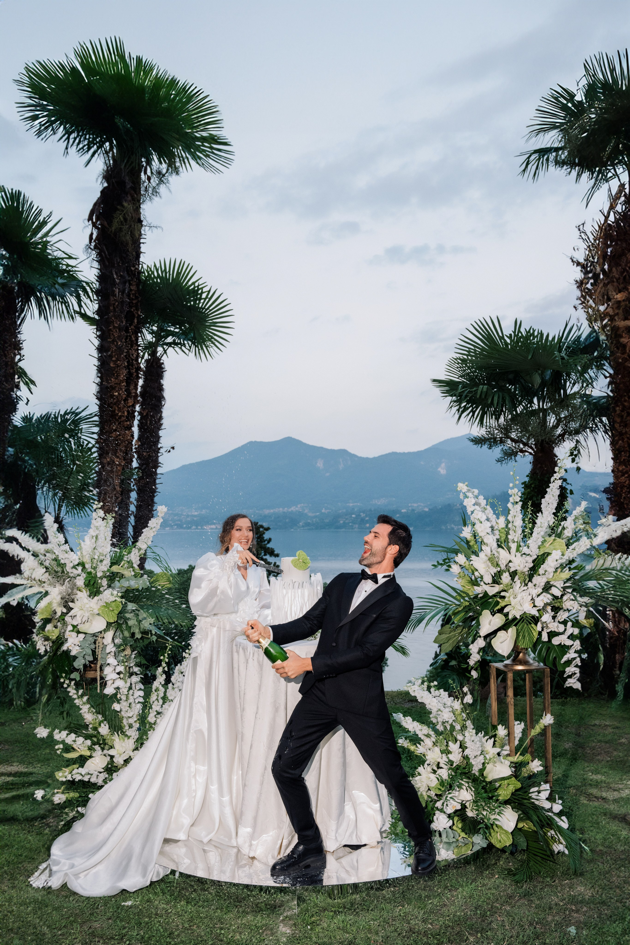 a bride and groom sitting on a lawn with palm trees
