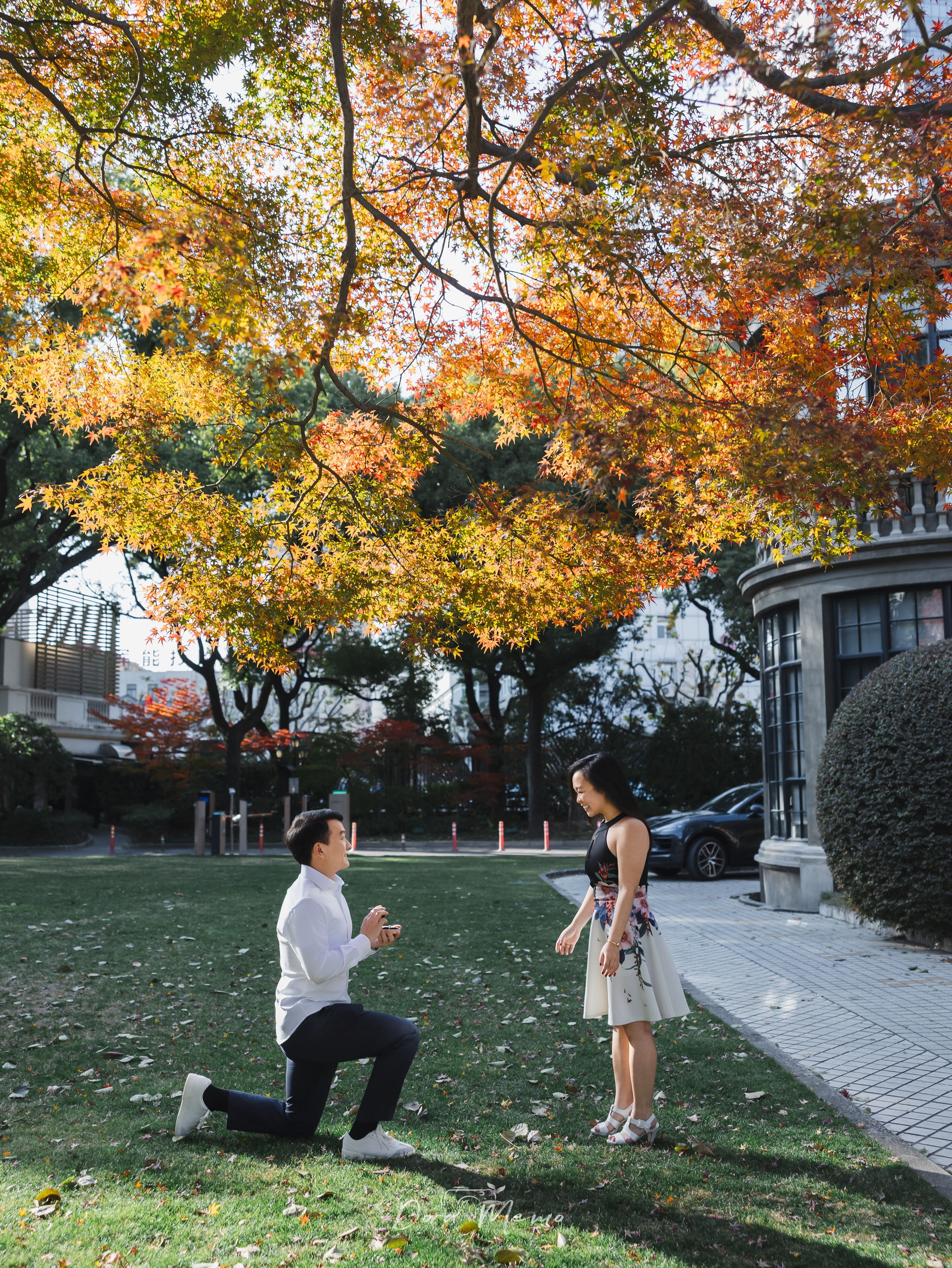 Groom-to-be on one knee framed by red maple leaves during a Shanghai engagement