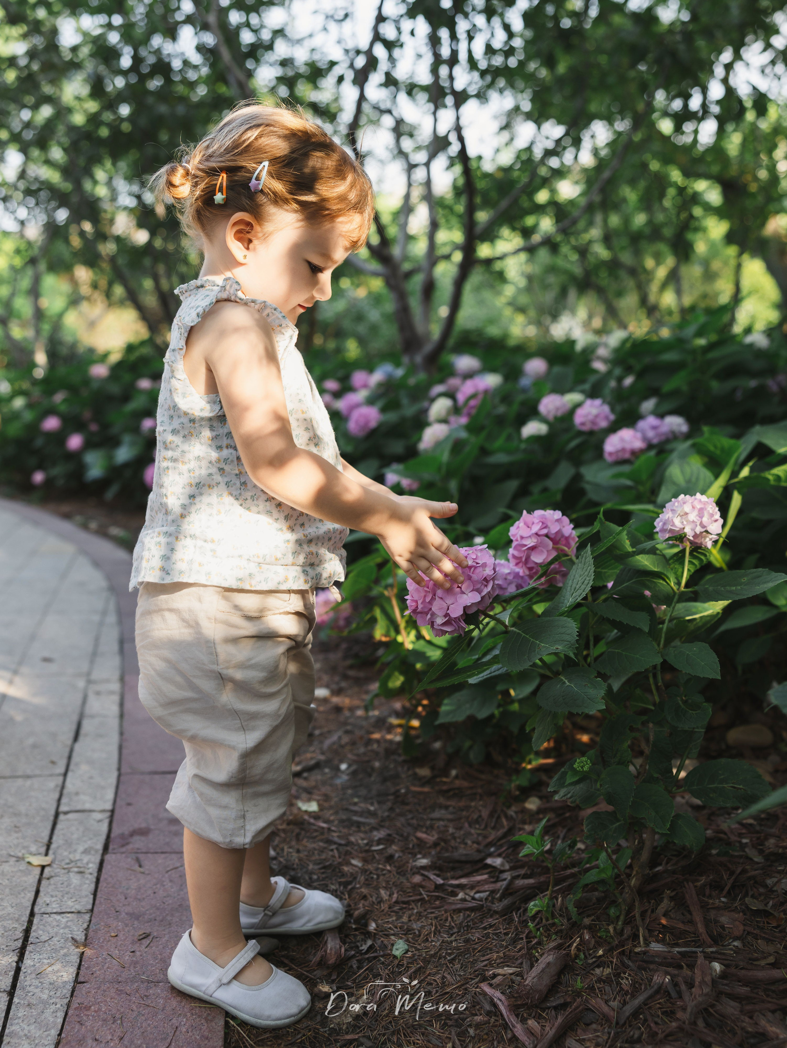 Toddler daughter gently touching a pink flower | A toddler curiously touching a pink flower, quiet moment of childhood wonder