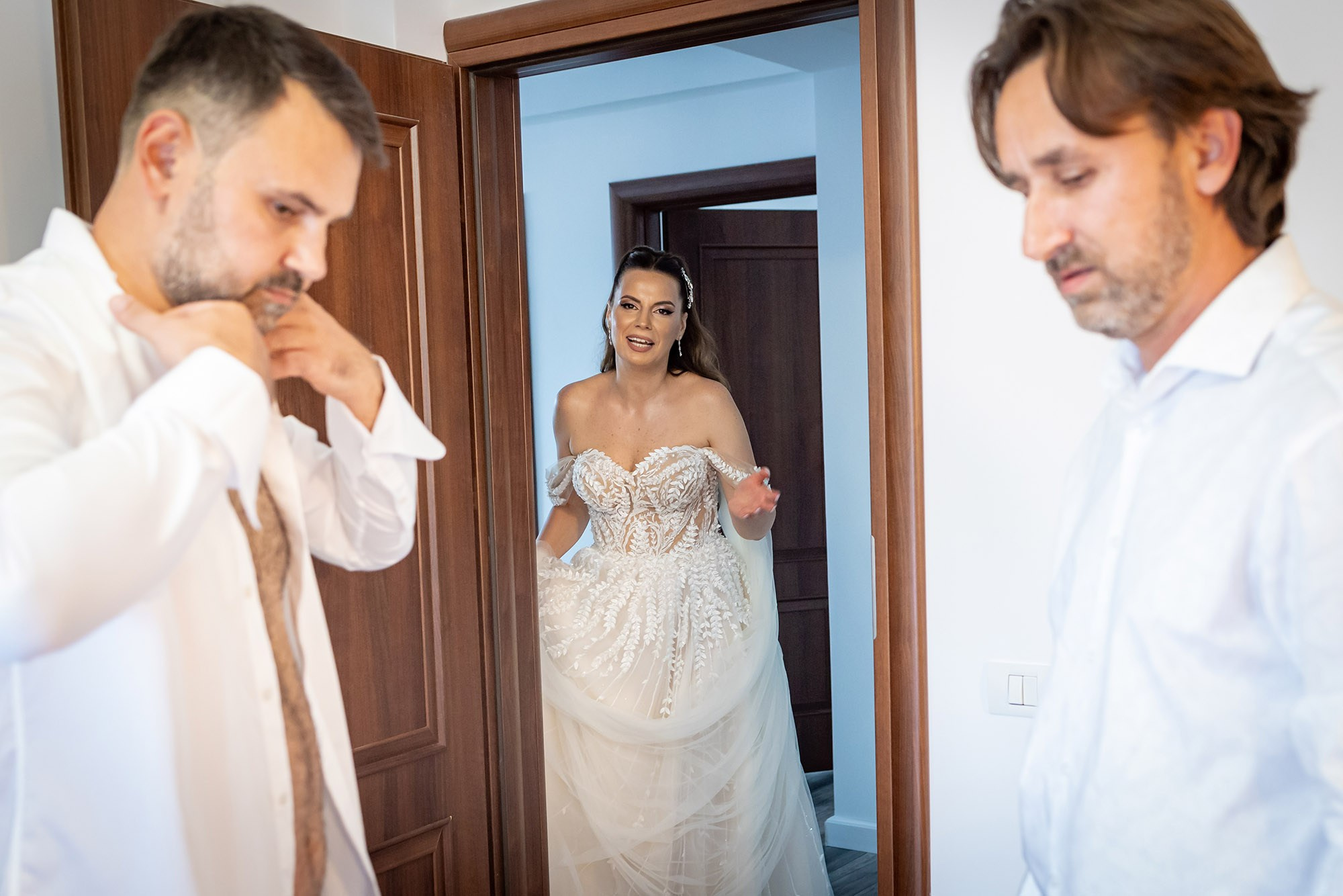  Mireasă în rochie albă cu broderie apare în ușă și îl surprinde pe mire în timp ce se pregătește