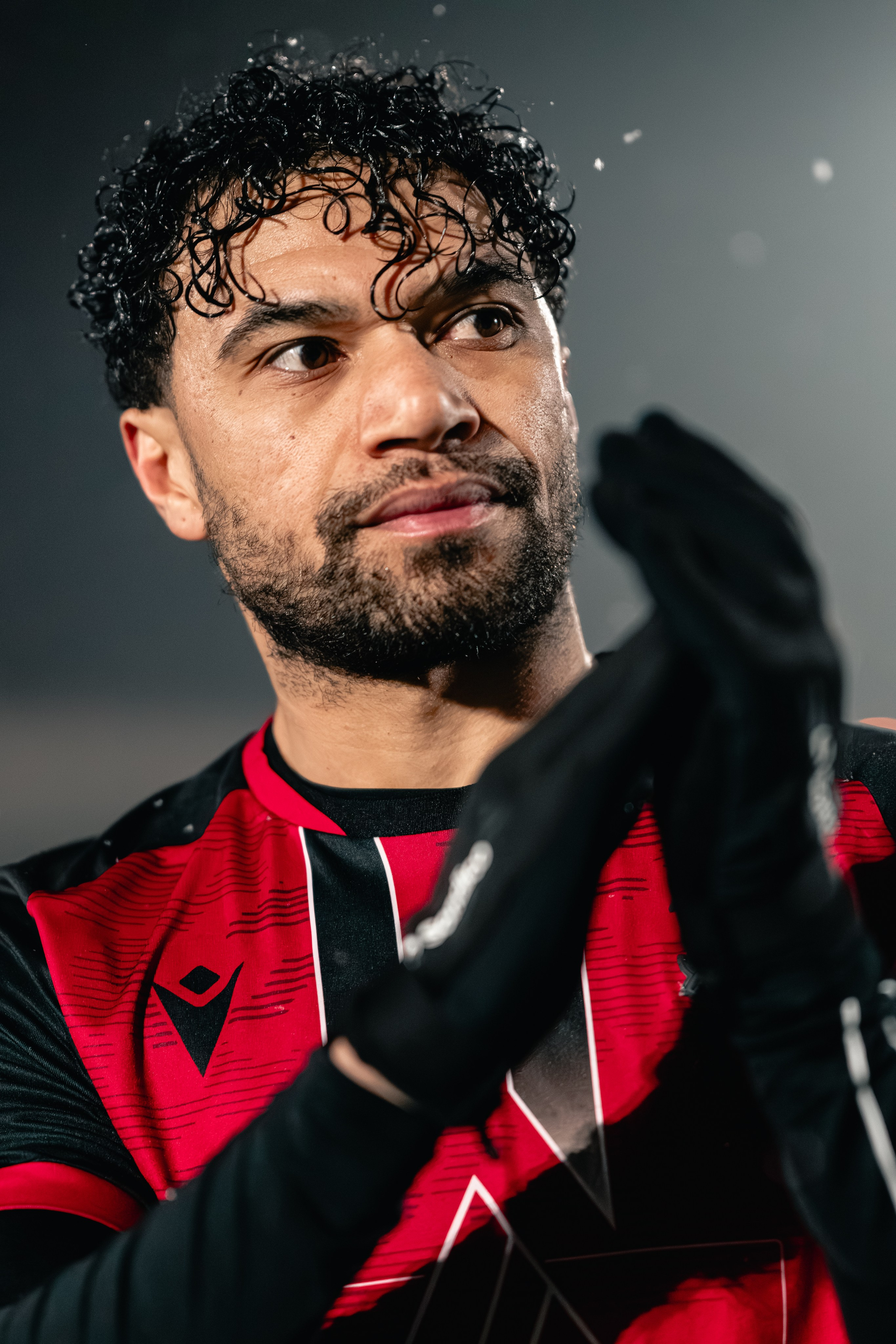 Close-up of Luke Fairlamb in a Tamworth FC red shirt applauding under the floodlights in falling rain during the Birmingham Senior Cup tie vs Alvechurch at The Lamb Ground, Feb 3 2026.