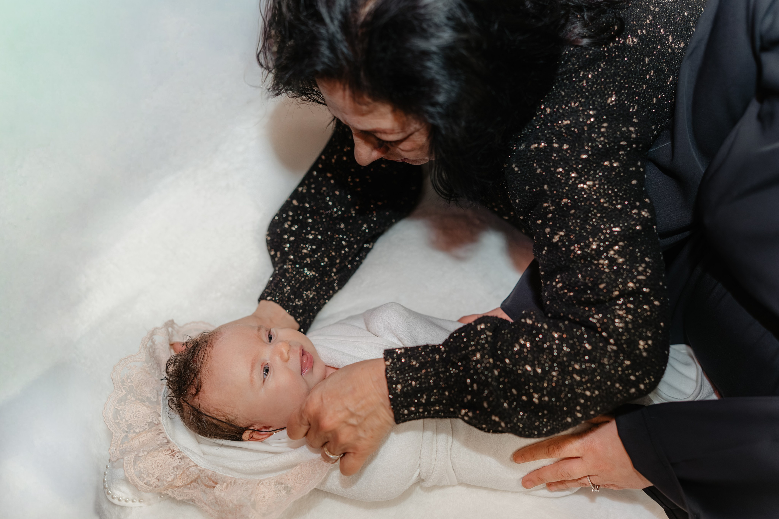 După ceremonie, moașa (nașa) îngrijește și se joagă cu pruncul Eveline Maria pe masa de botez, ștergându-l cu prosopul și râzând cu el. Un moment de bucurie și afecțiune spontană.