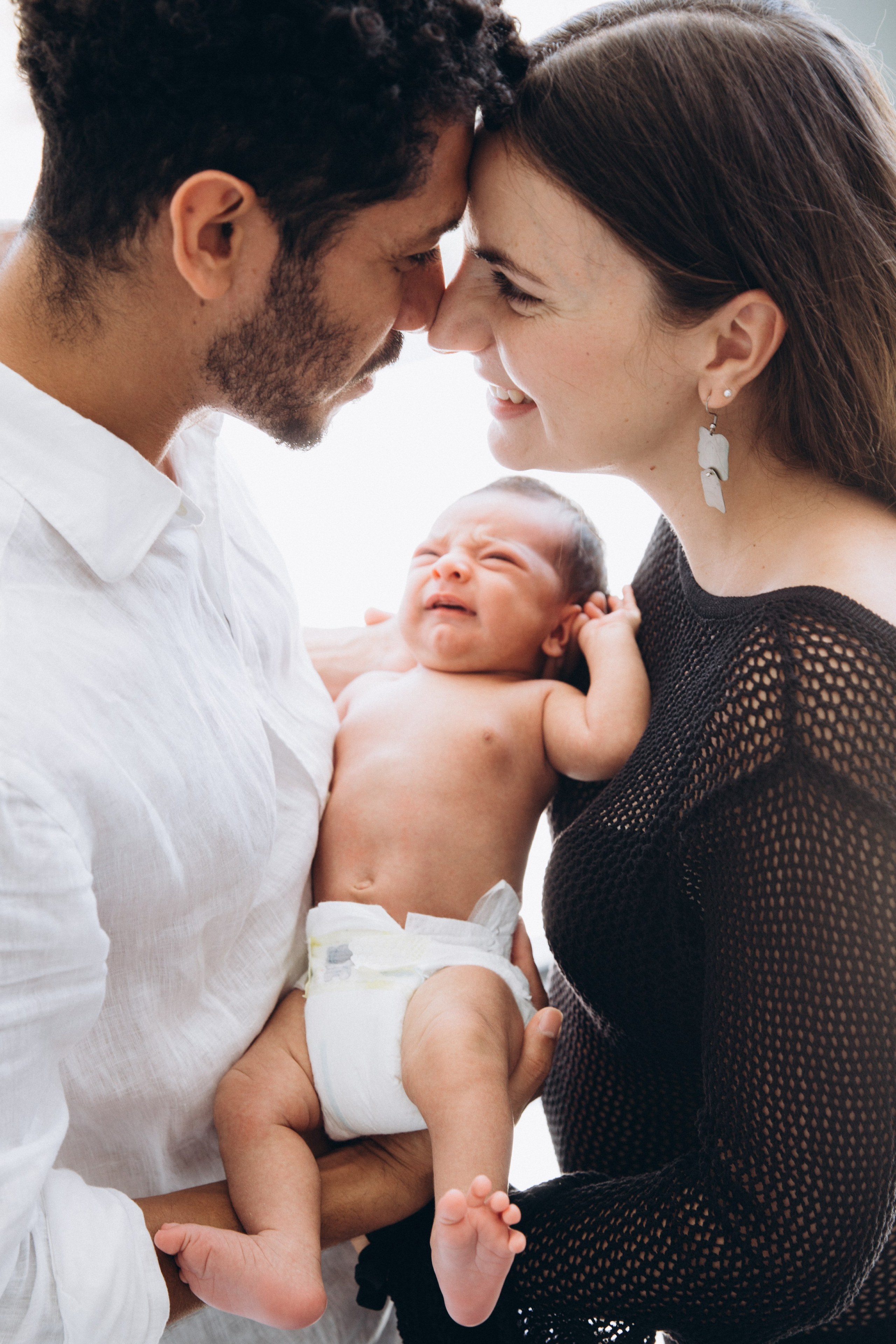 Retrato familiar tierno tomado en Alicante, España — padres compartiendo un momento íntimo mientras sostienen a su bebé recién nacido, capturando hermosamente el amor y el vínculo inicial. Ideal para quienes buscan sesiones de fotos familiares y de recién nacidos naturales y emotivas en Alicante y en toda España.