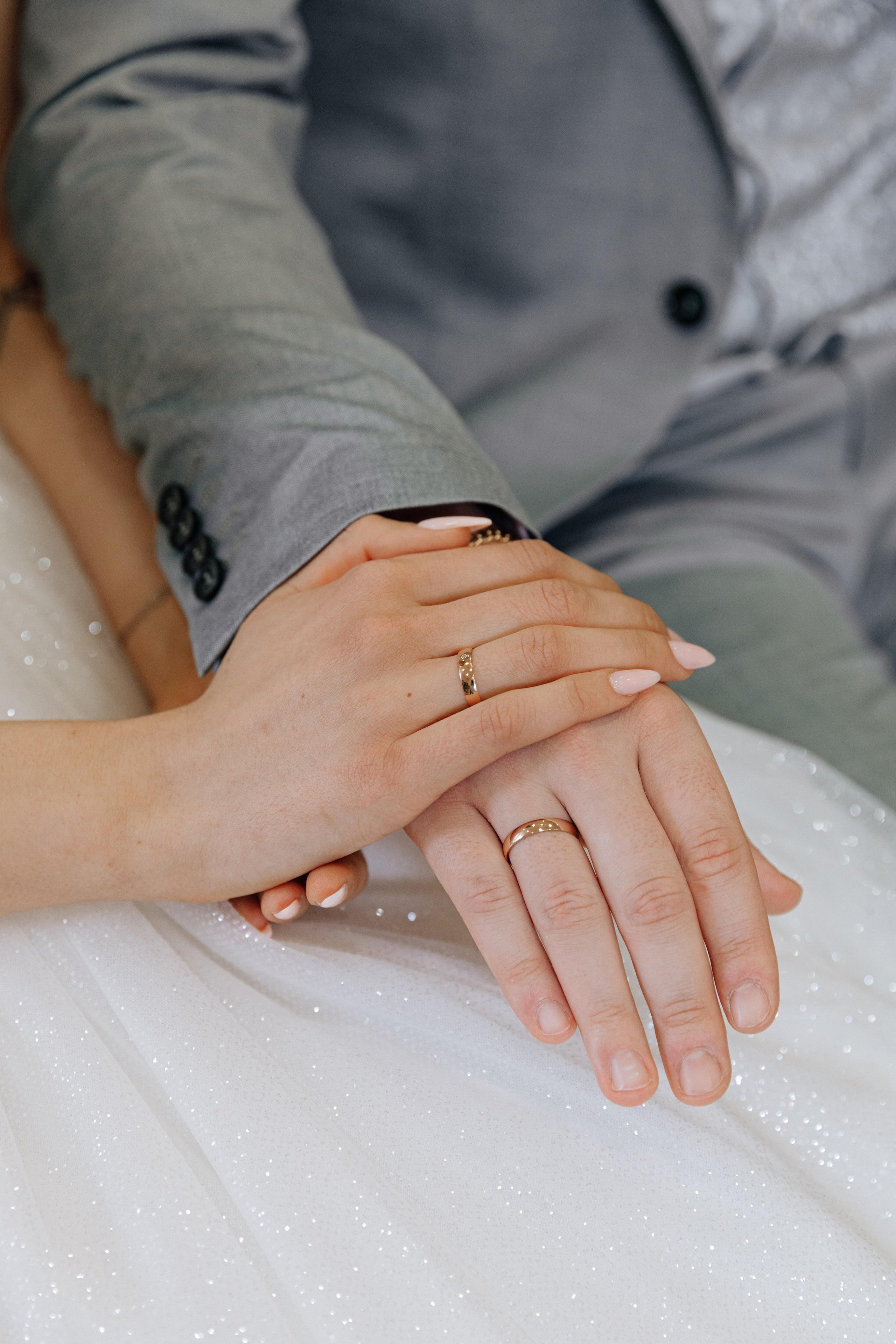 Die Hand der Braut liegt auf der Hand des Bräutigams, wobei die Eheringe sichtbar sind. Ein symbolischer Moment der Hochzeitszeremonie.