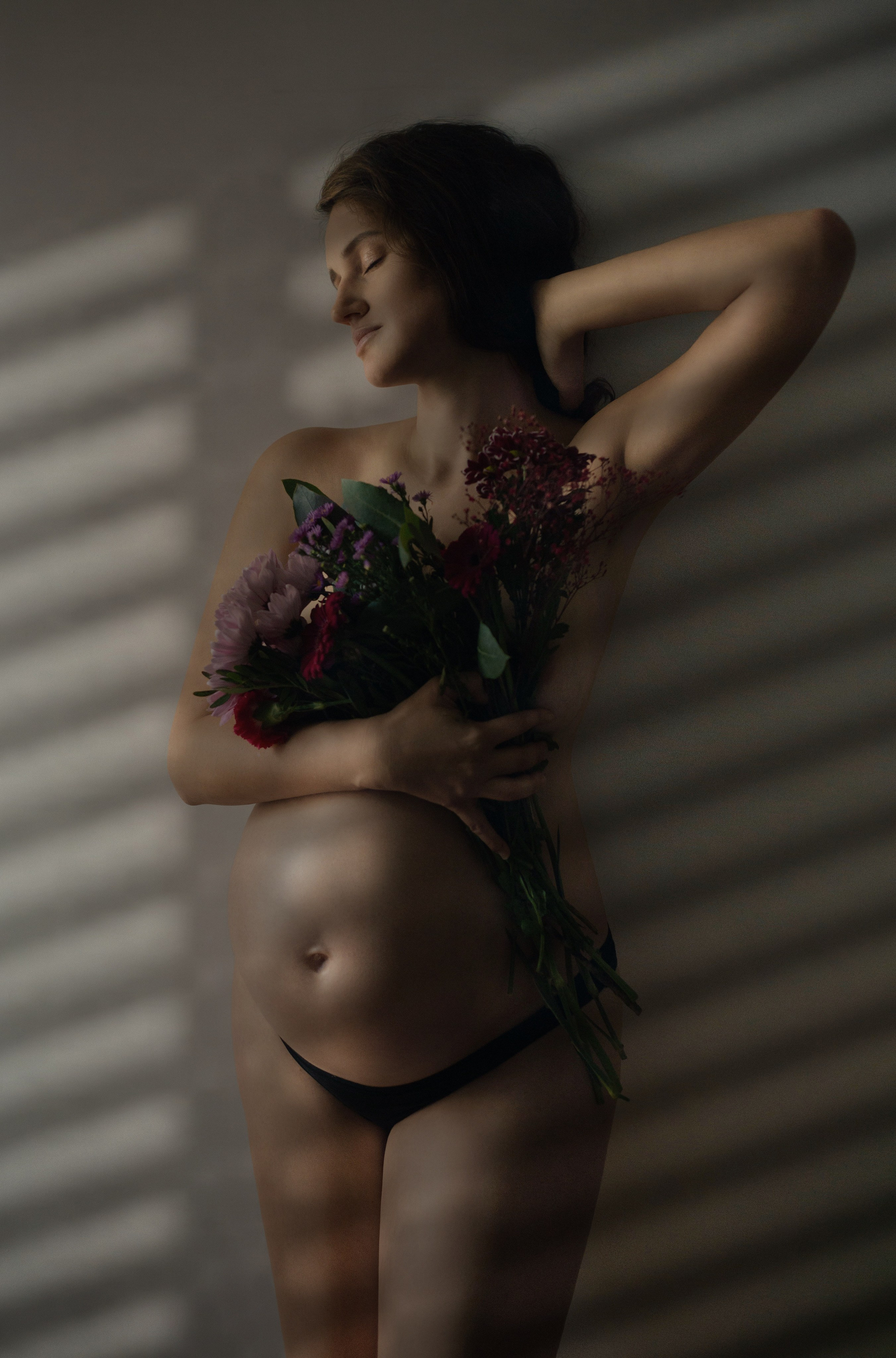 Silhouette artistique d'une femme enceinte en contre-jour avec lumière à travers les stores