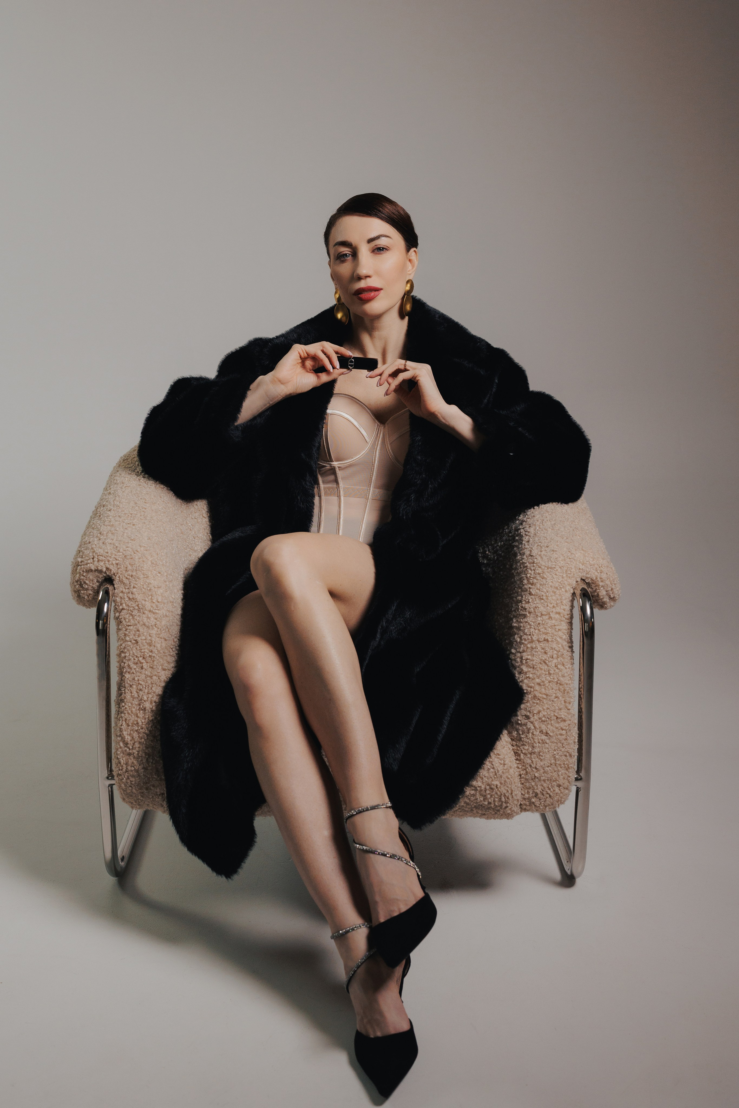 Editorial fashion portrait of a woman in a black fur coat sitting in a chair with elegant posture and cinematic lighting, photographed in Leipzig, Germany. Редакционный фэшн-портрет девушки в чёрной шубе, сидящей в кресле в элегантной позе с кинематографичным светом, снятый в Лейпциге, Германия.