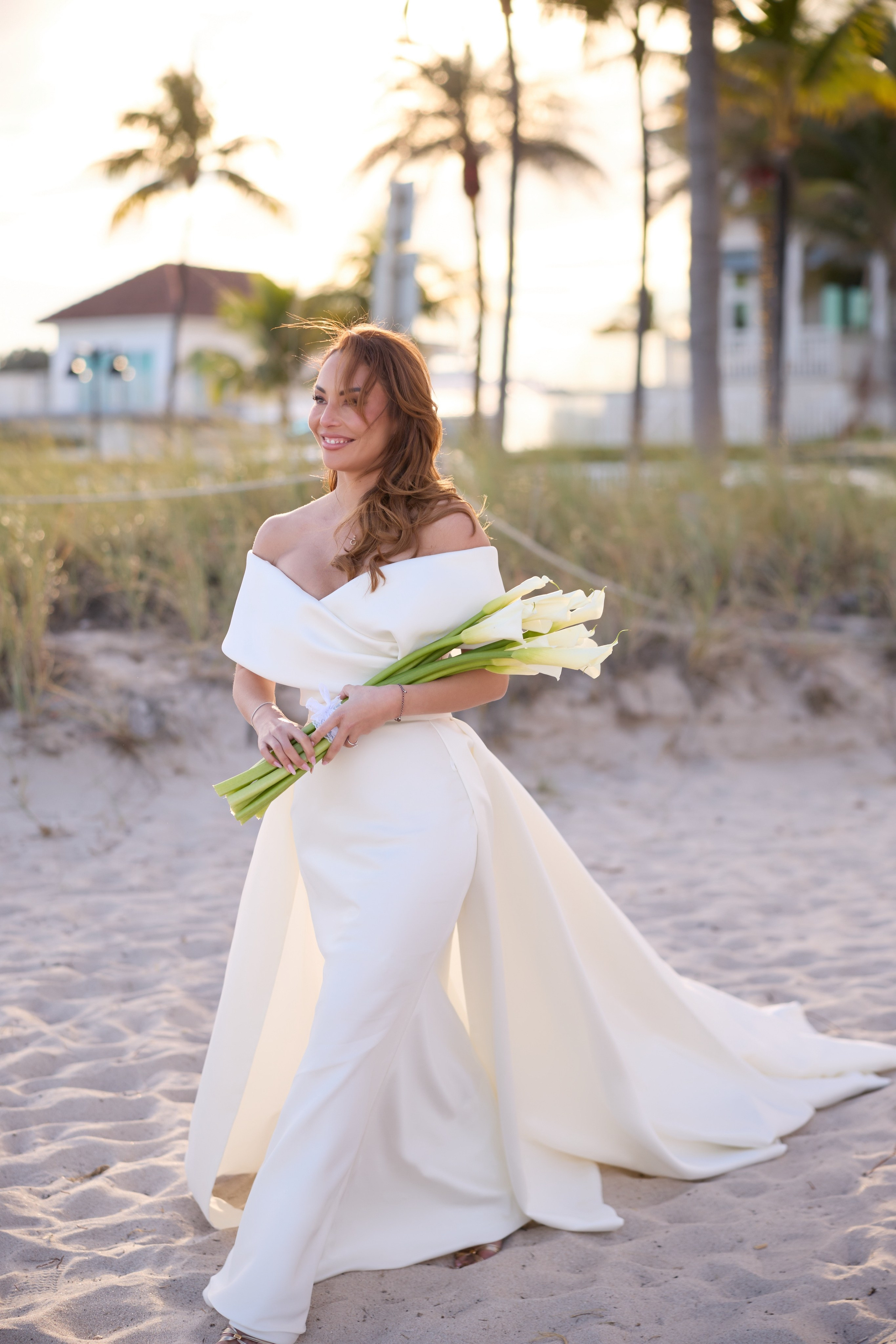 Elegant bride holding white calla lilies on a sunlit beach