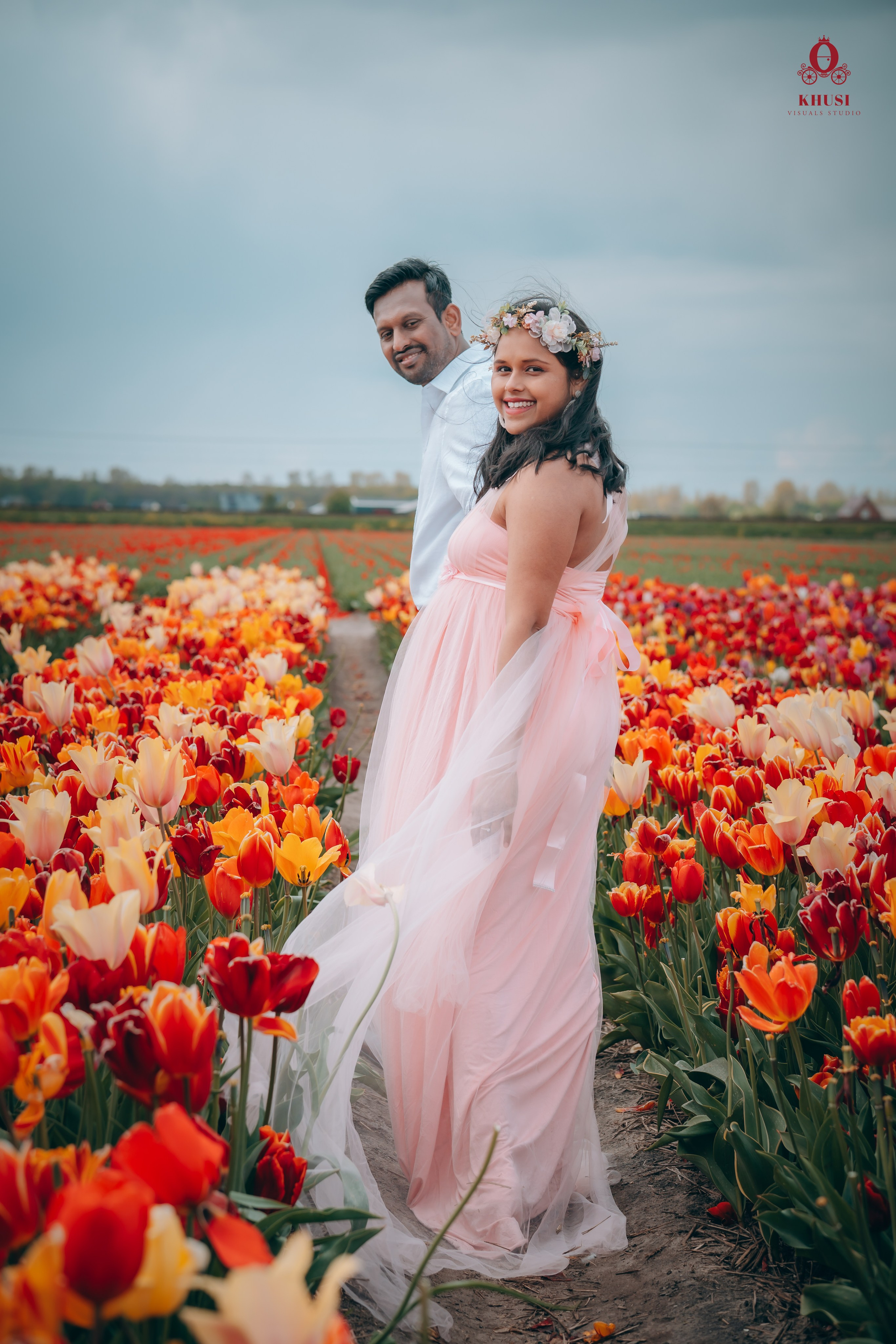 A man holding the hand of his pregnant wife and walking in a tulip fields in netherlands