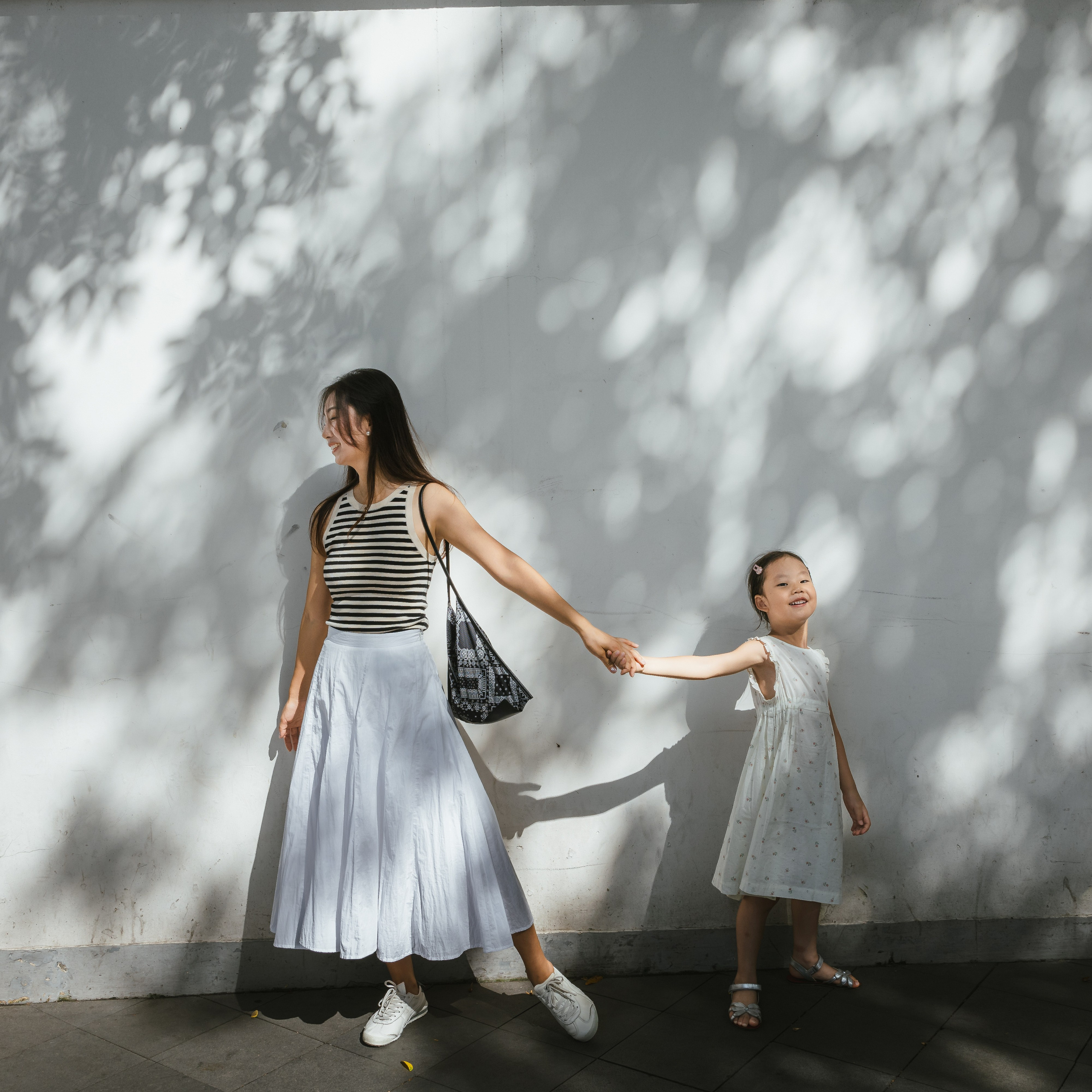 A mother and 6-year-daughter playing on Wukang Road, shanghai,  with dappled light and shadows in the background.