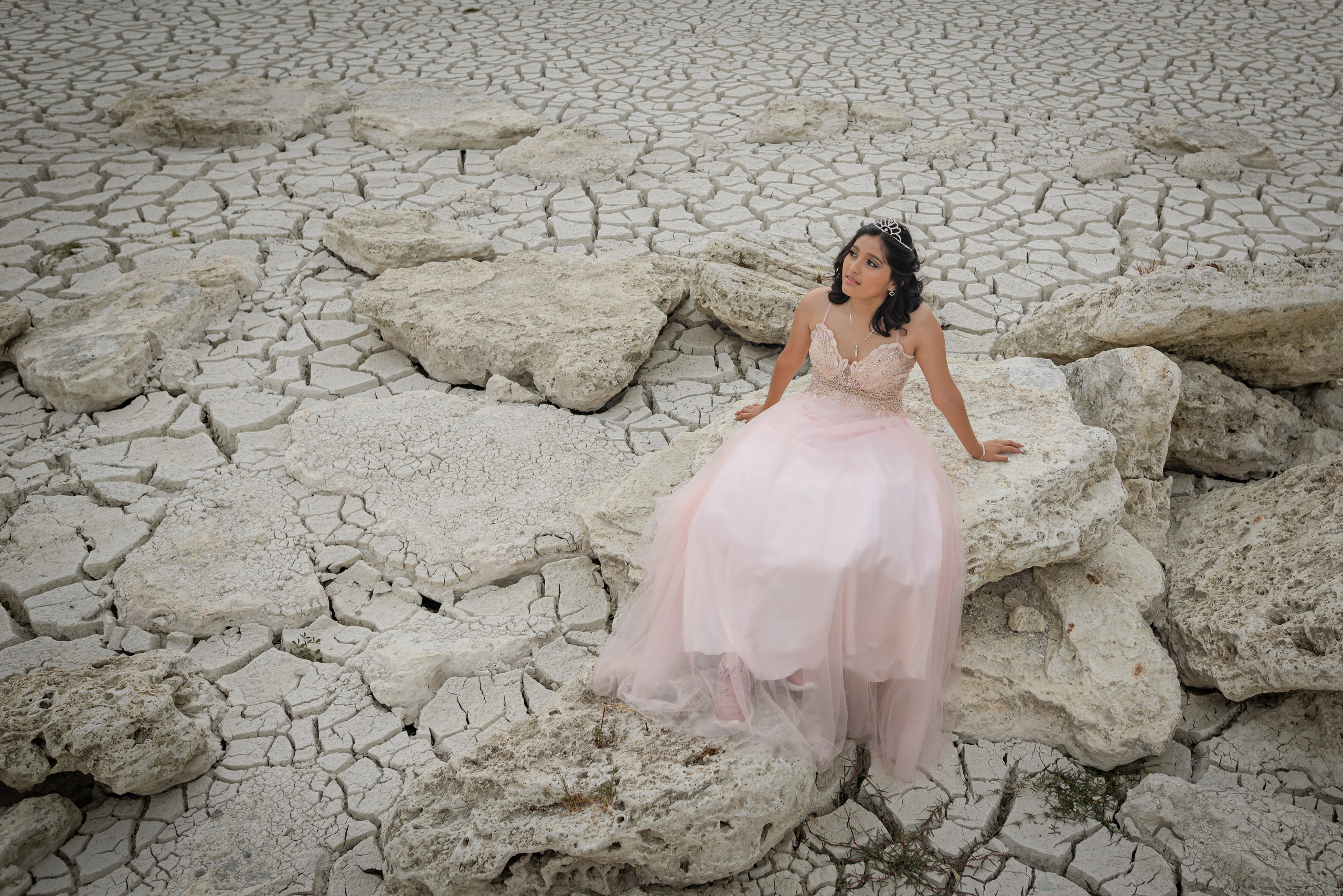 Michelle in a pink dress surrounded by cracked dry land, desert textures, and dramatic arid scenery, captured by destination portrait photographer