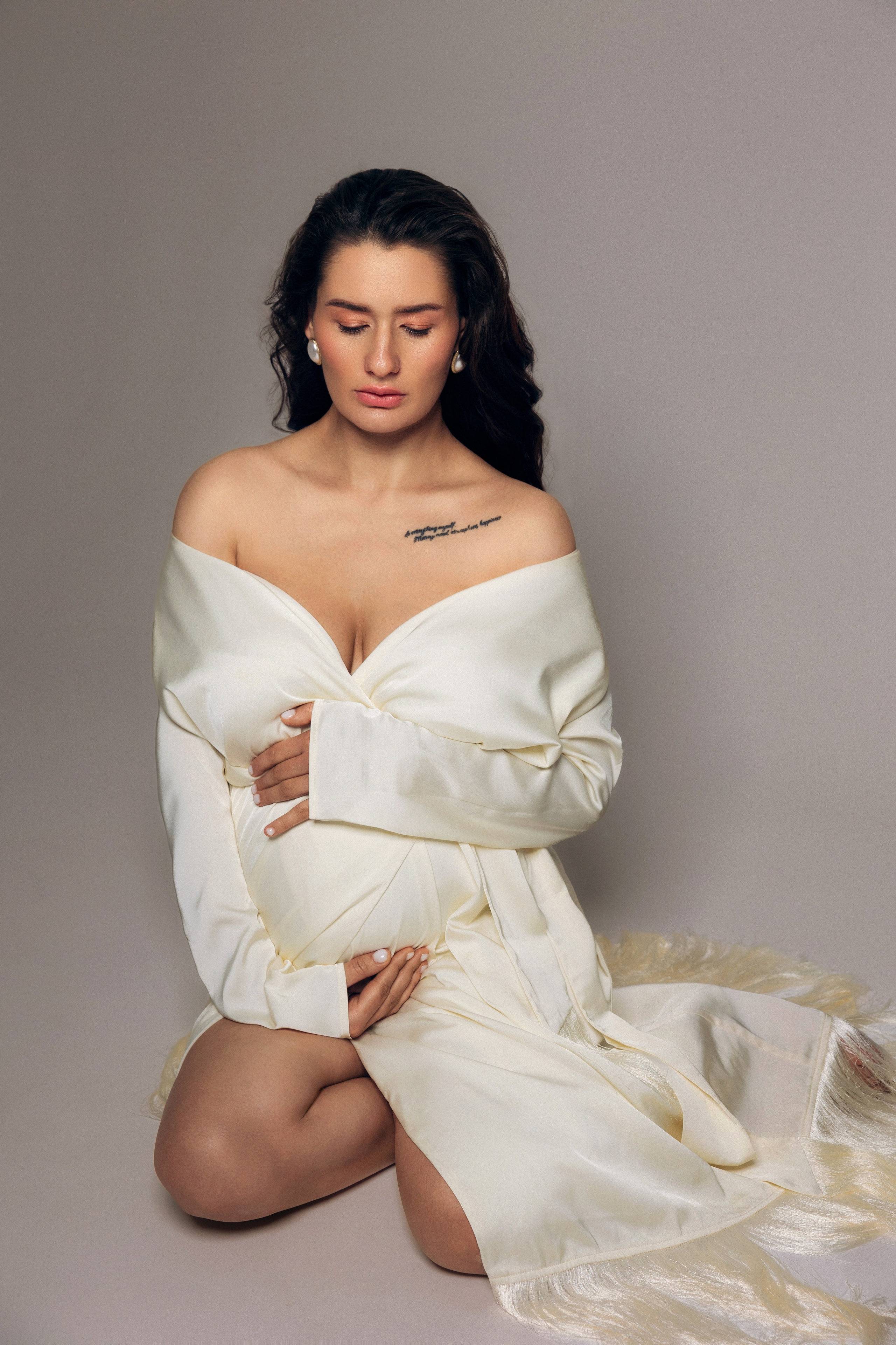 Sesja ciążowa w studio Prostir – kobieta siedzi na podłodze, dłonie na brzuchu, subtelna stylizacja i spokój. Maternity session at Prostir studio – woman sitting on the floor, hands on belly, subtle styling and calm vibe.