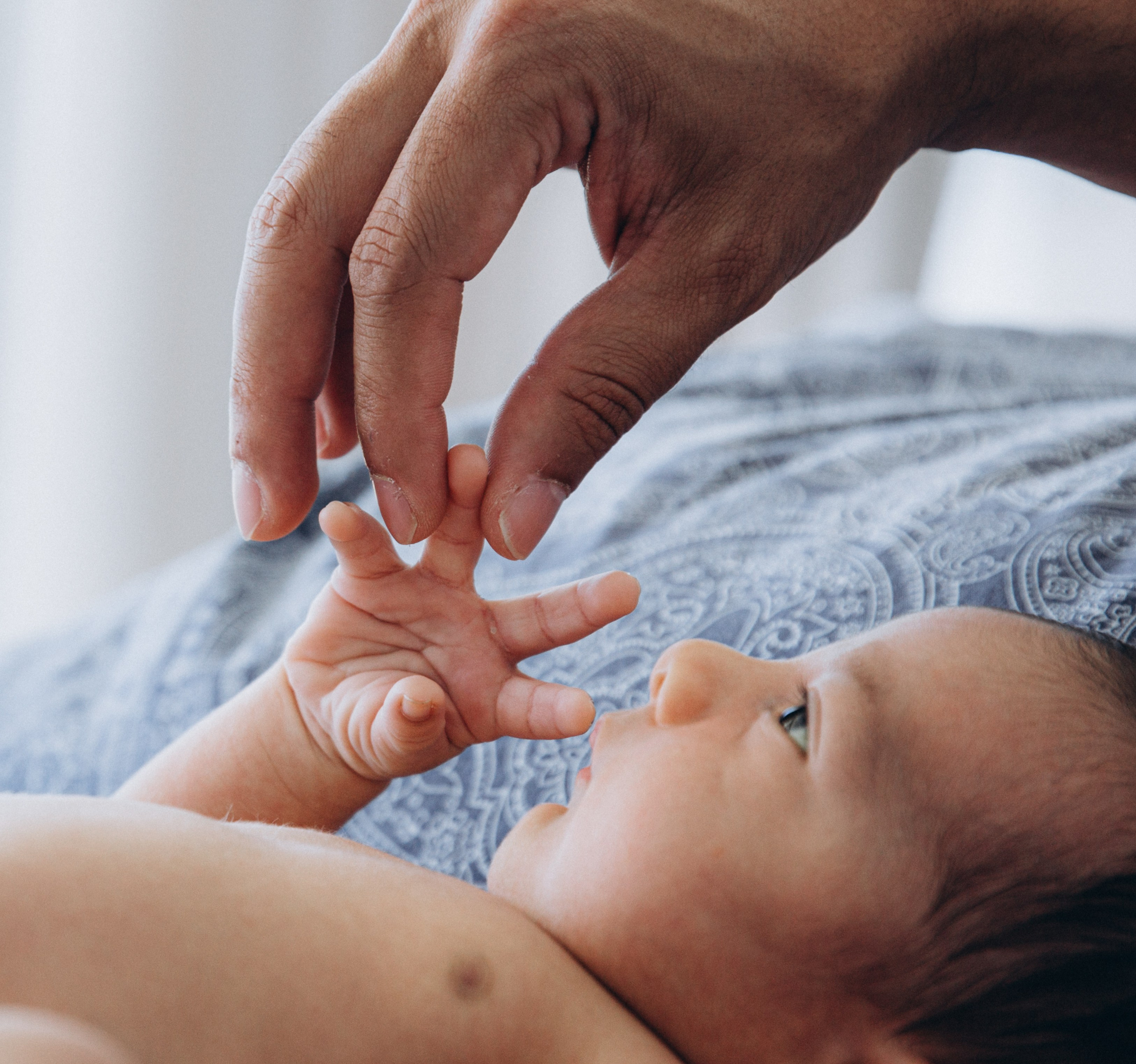 Tierno instante de padre y bebé en Denia, España — recién nacido sujetando con su manita el dedo del padre sobre una manta suave.