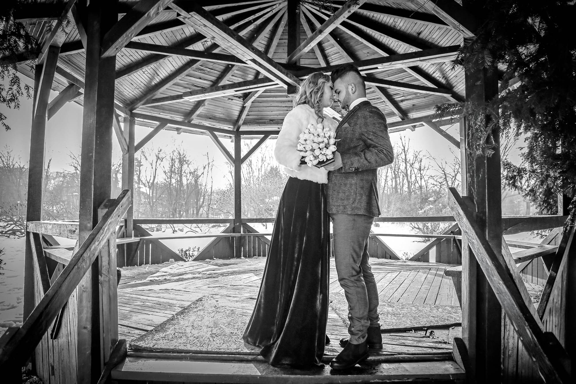 Newlyweds captured in a black and white close shot inside the rustic gazebo, highlighting the details of their elegant winter attire.