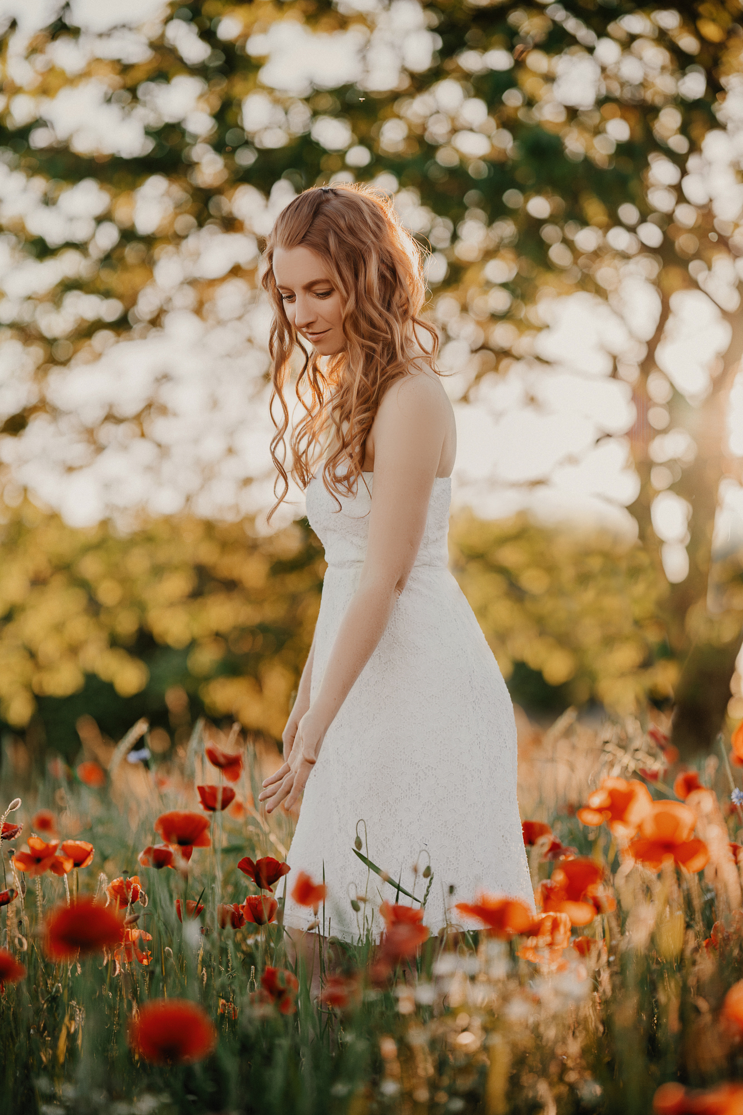 Rothaarige junge Frau im weißen Kleid im Mohnfeld