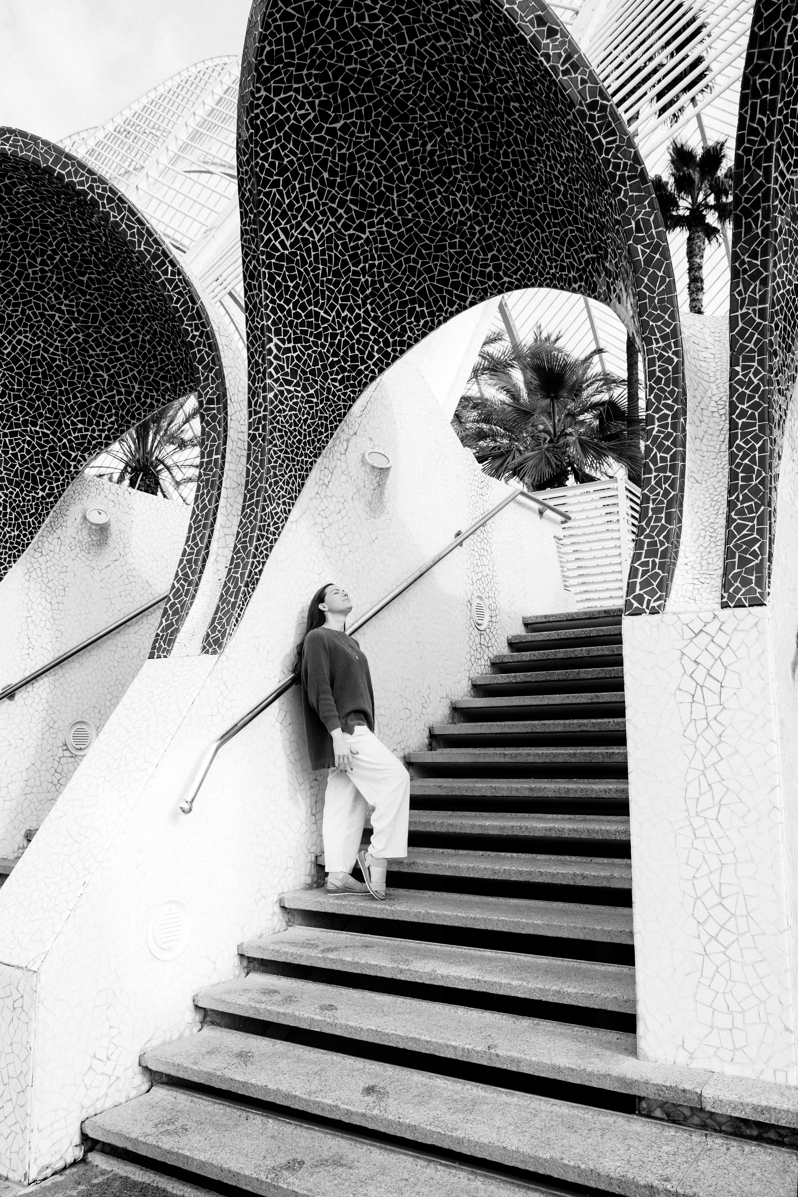 Женская портретная фотосессия в Валенсии, Испания: женщина поднимается по изящной архитектурной лестнице с изогнутыми арками, снято в черно-белом стиле для создания художественной и вневременной композиции — идеально для креативной женской портретной фотографии и fine art фотосессий.