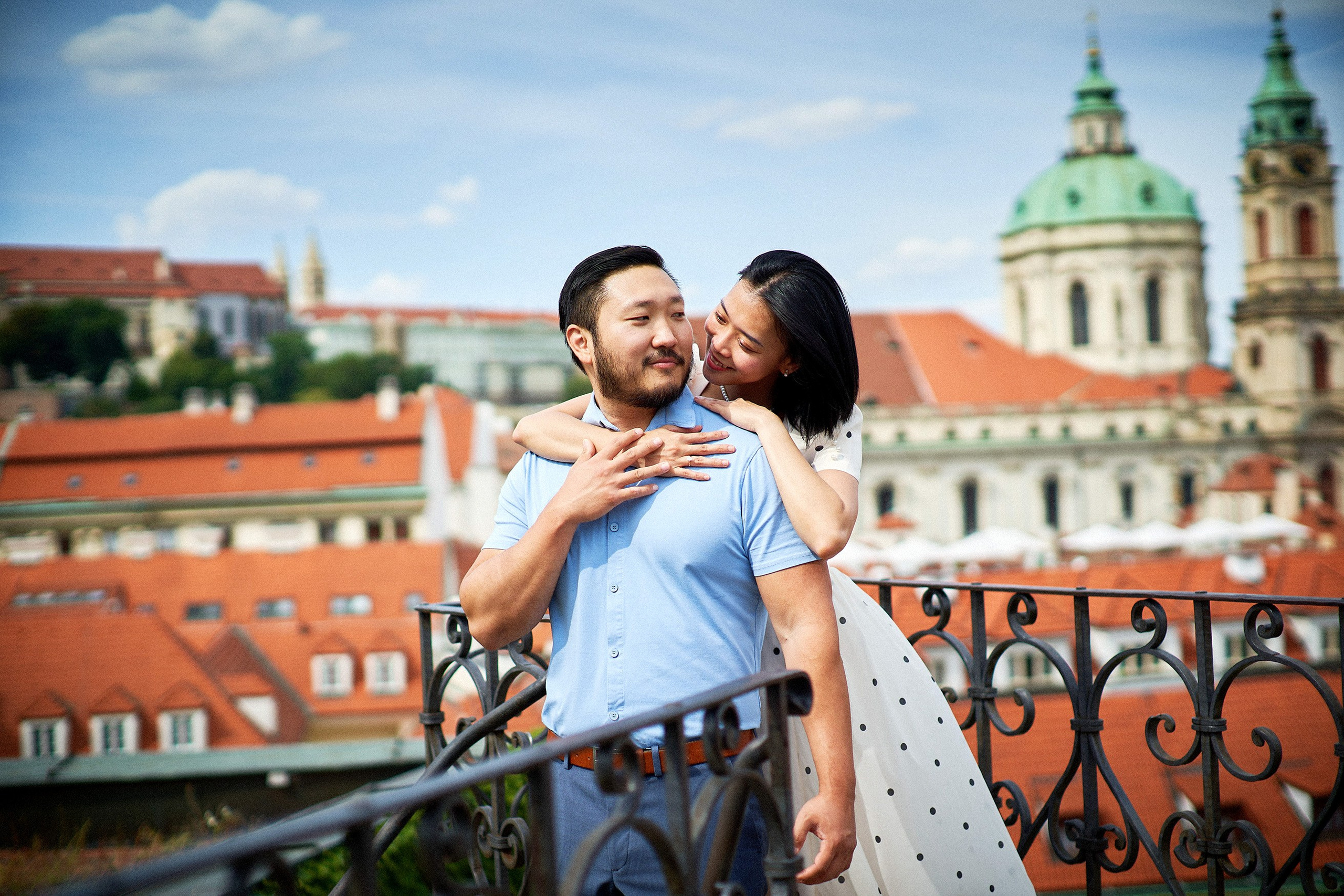 Woman standing behind her fiancé and whispering in his ear in Vrtba Garden, Prague.