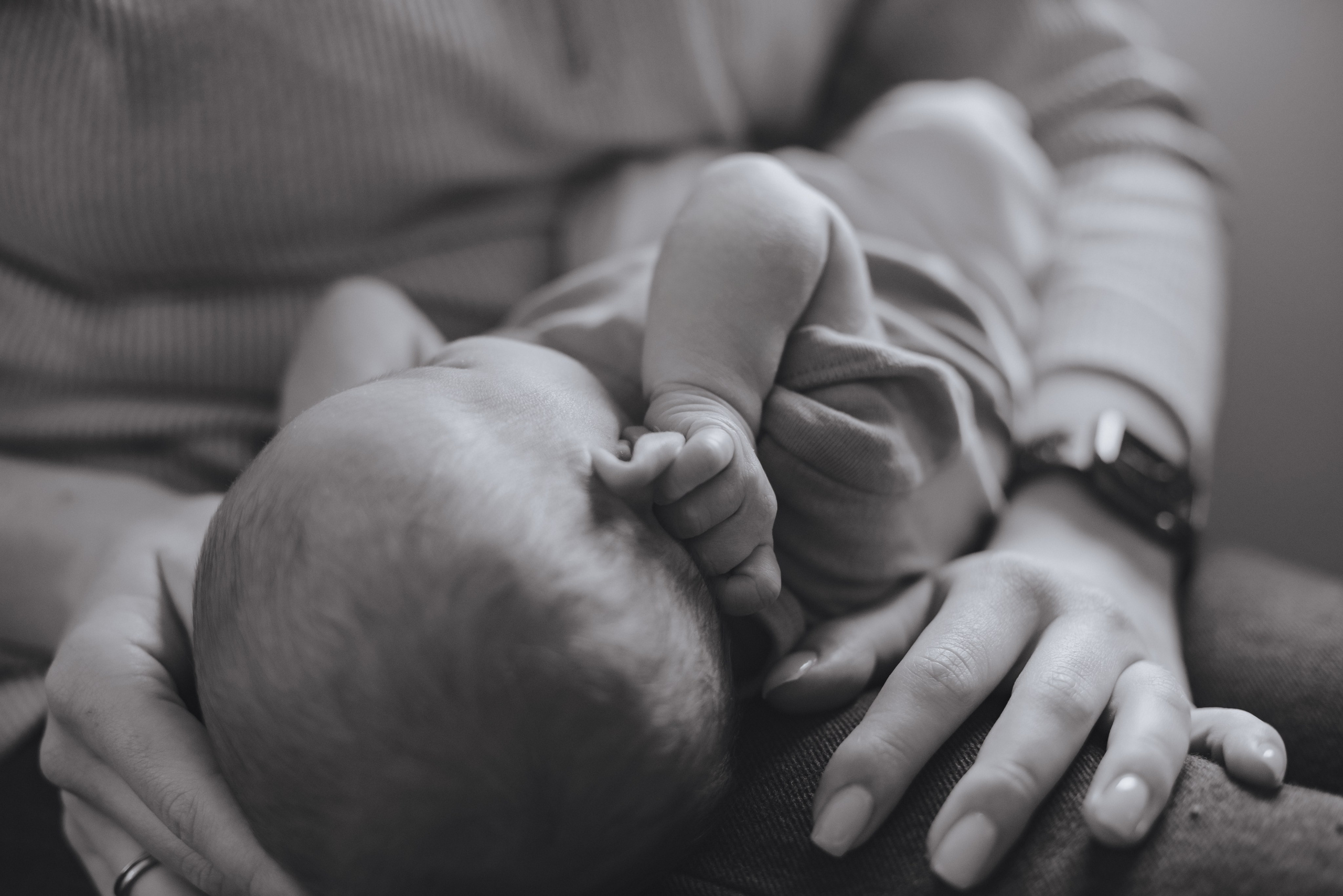 Neugeborenes hält sich mit kleinen Händchen an den Ohren fest. Ein zarter und niedlicher Moment.