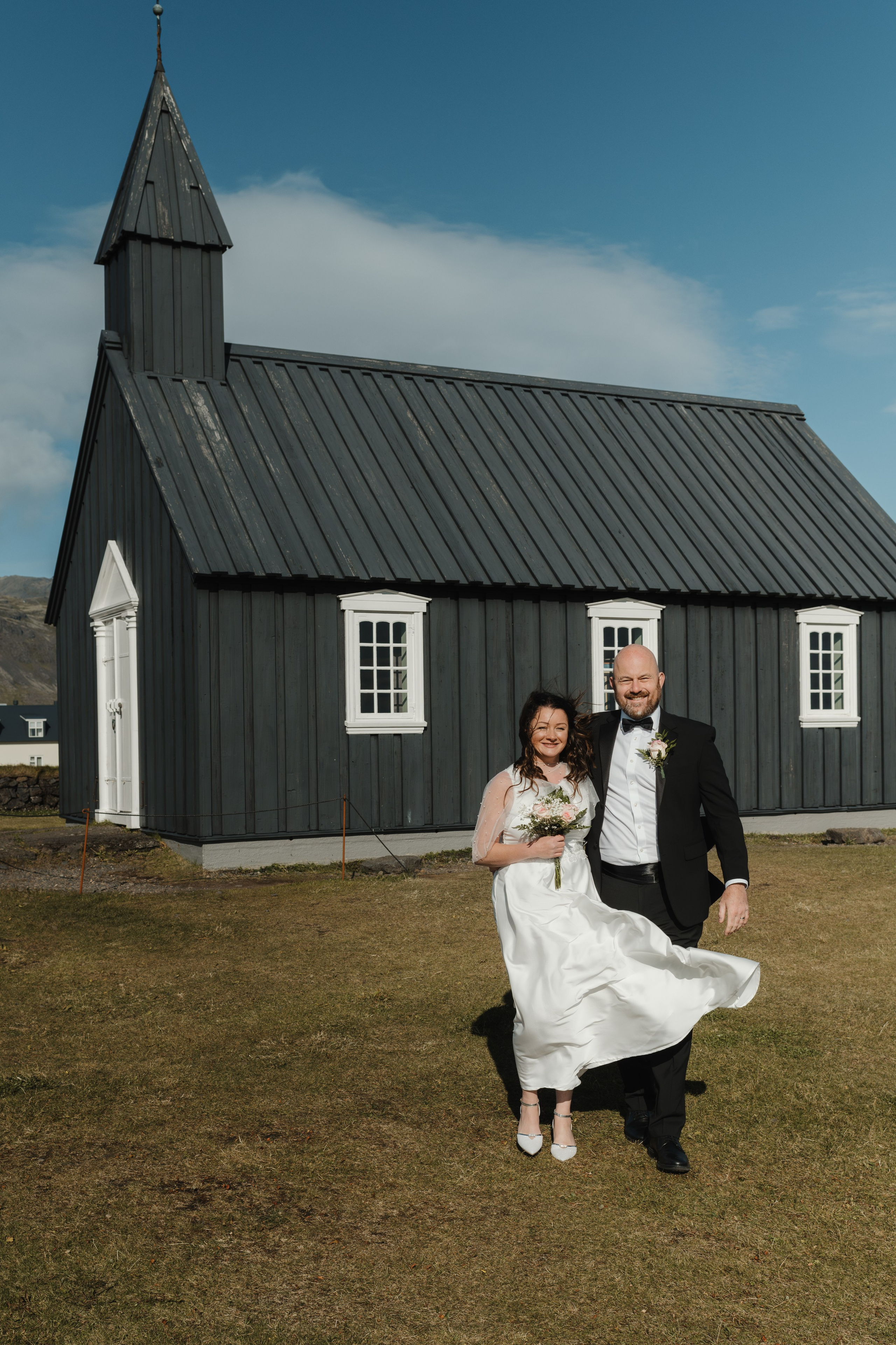 Bride and groom standing in front of the iconic black Búðakirkja, with dramatic Icelandic skies above.