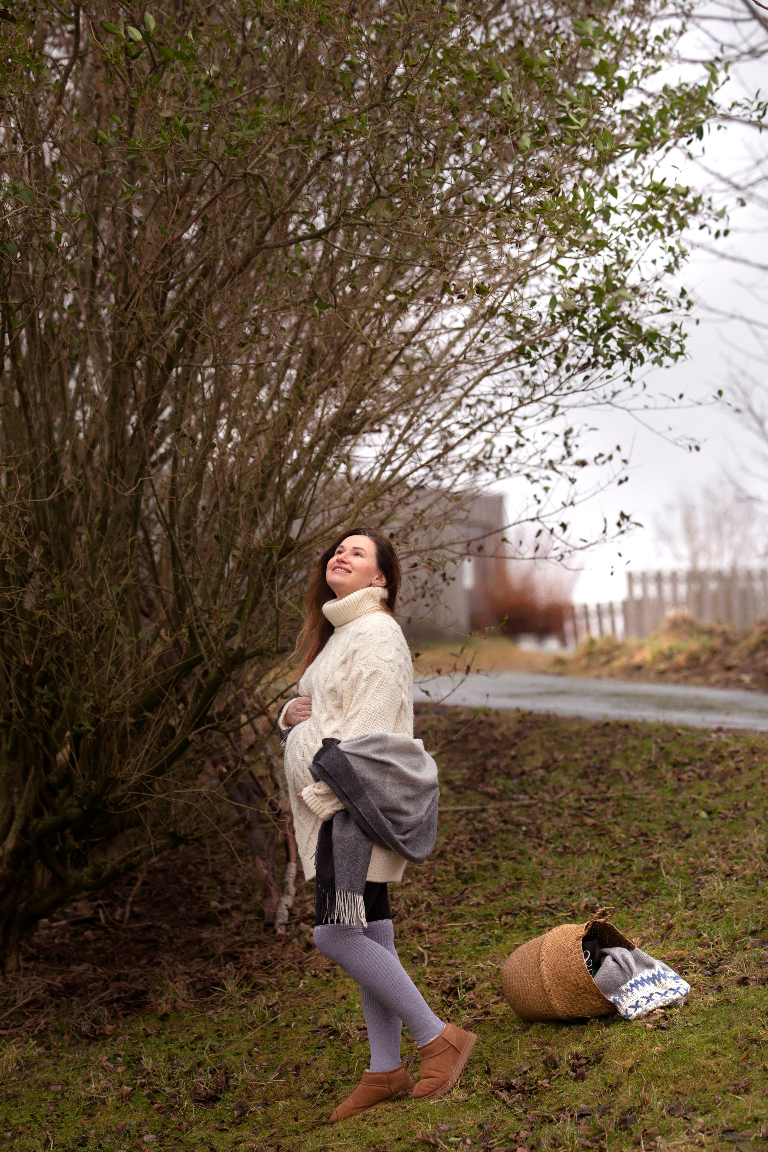 Pregnant woman standing by a tree in nude colors, embracing the natural beauty of maternity