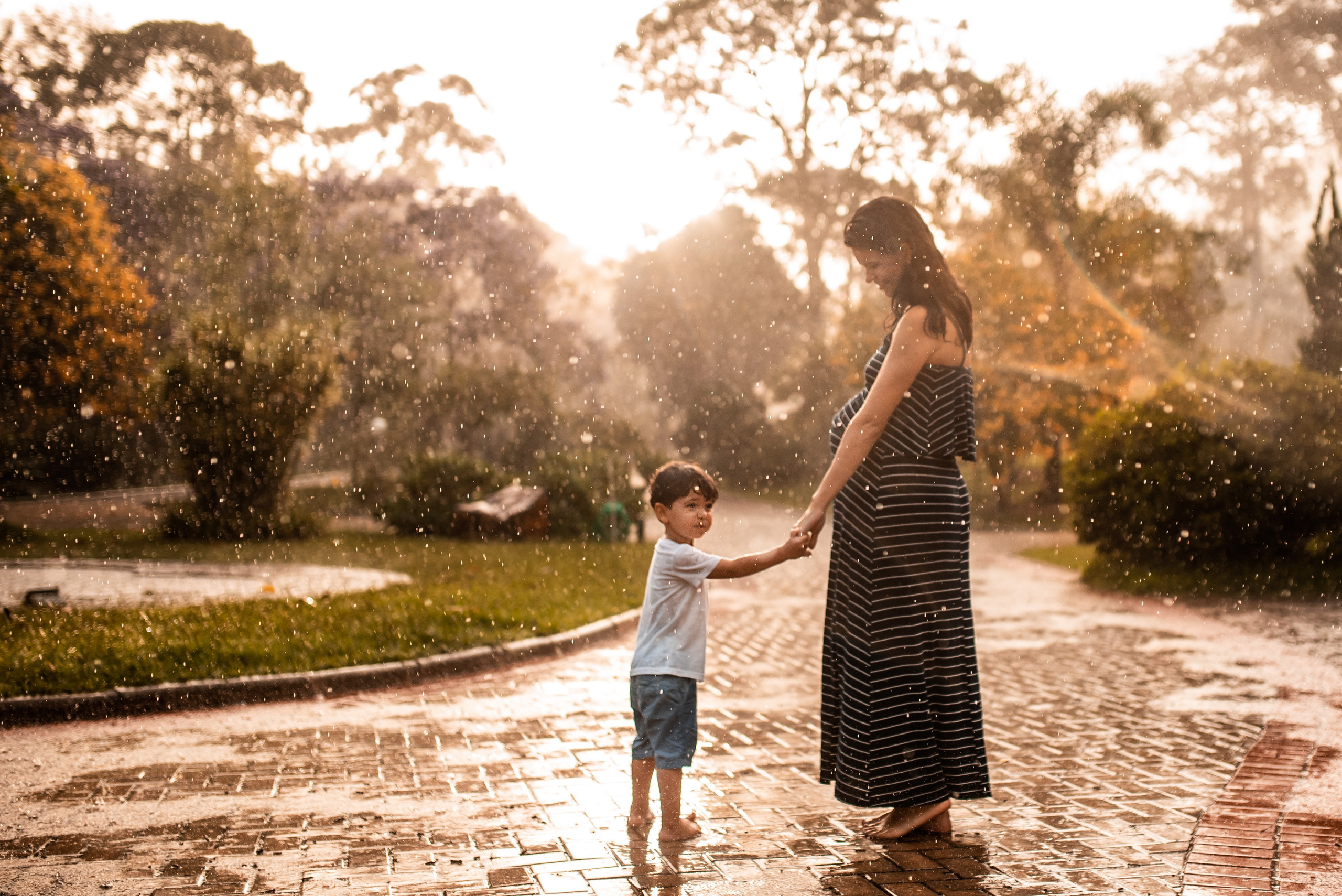Ensaio gestante ao ar livre em Juiz de Fora, mãe e filho de mãos dadas na chuva com luz dourada