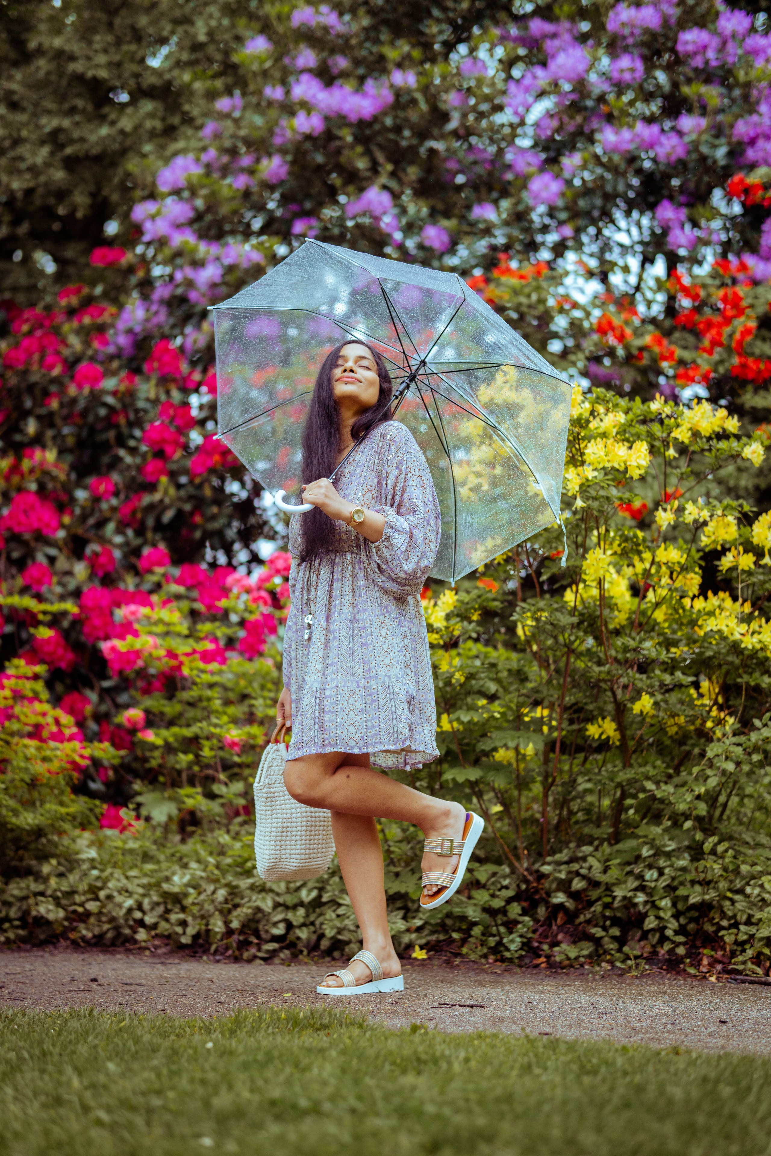 woman standing in a flower park and holding a transparent umbrella 