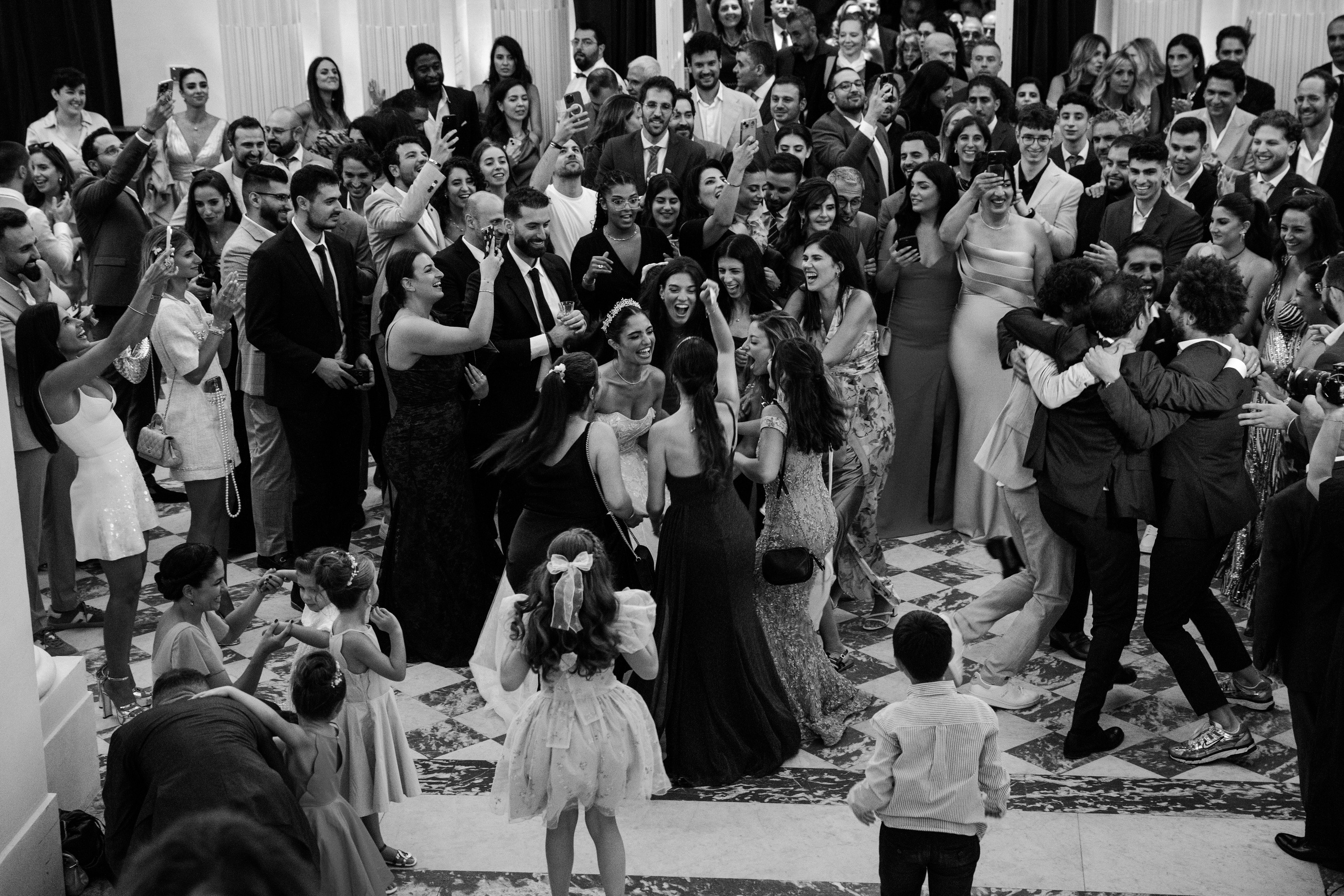 Joyful wedding reception in Paris with the bride surrounded by guests dancing and celebrating, captured in a candid documentary style