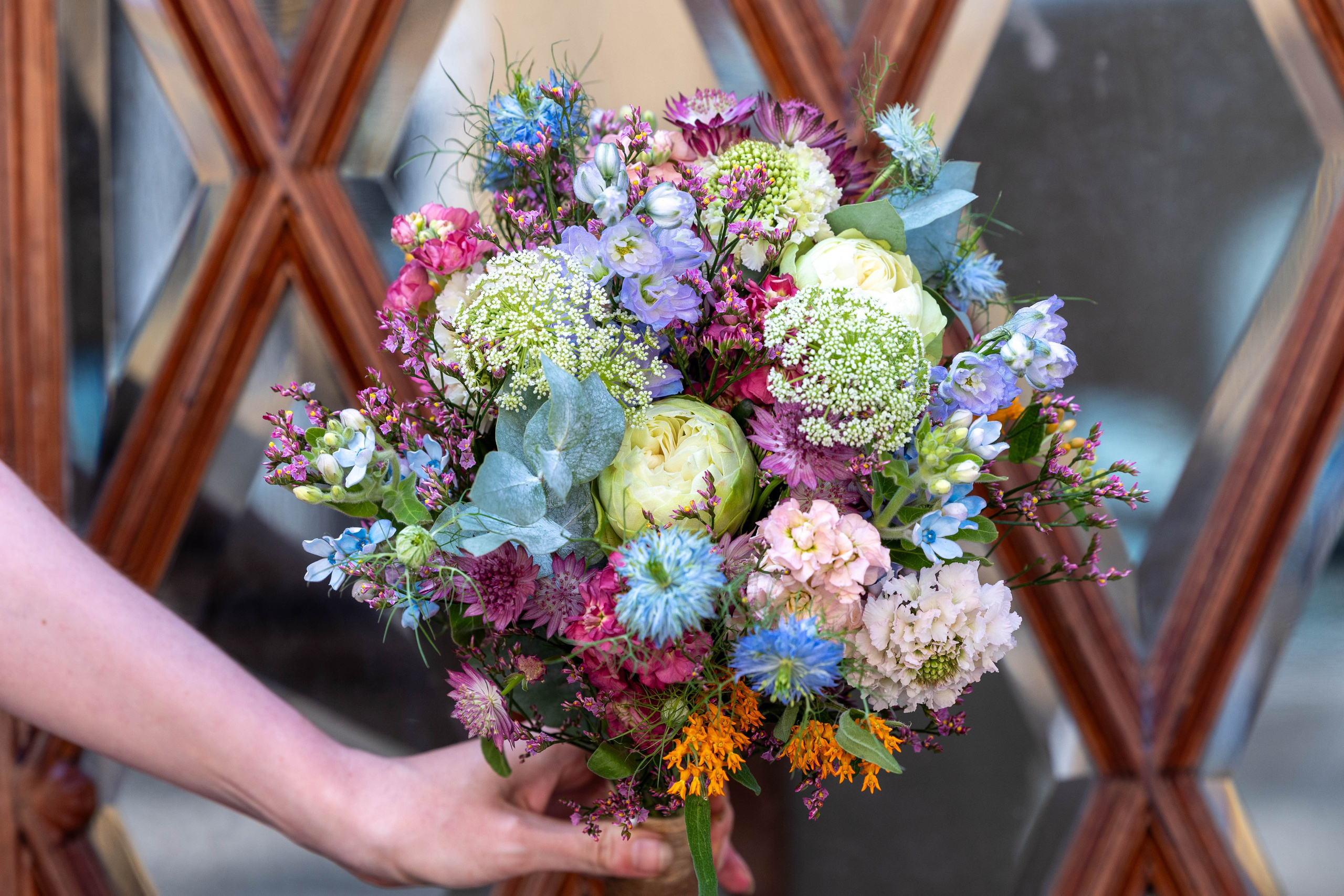 Brudebuket i en mere vild og naturlig stil, ofte omtalt som grøftekants- eller havestil. Denne buket bindes med korn og græsser, samt et udvalg af sæsonens blomster, og afsluttes altid med bast, medmindre andet ønskes.