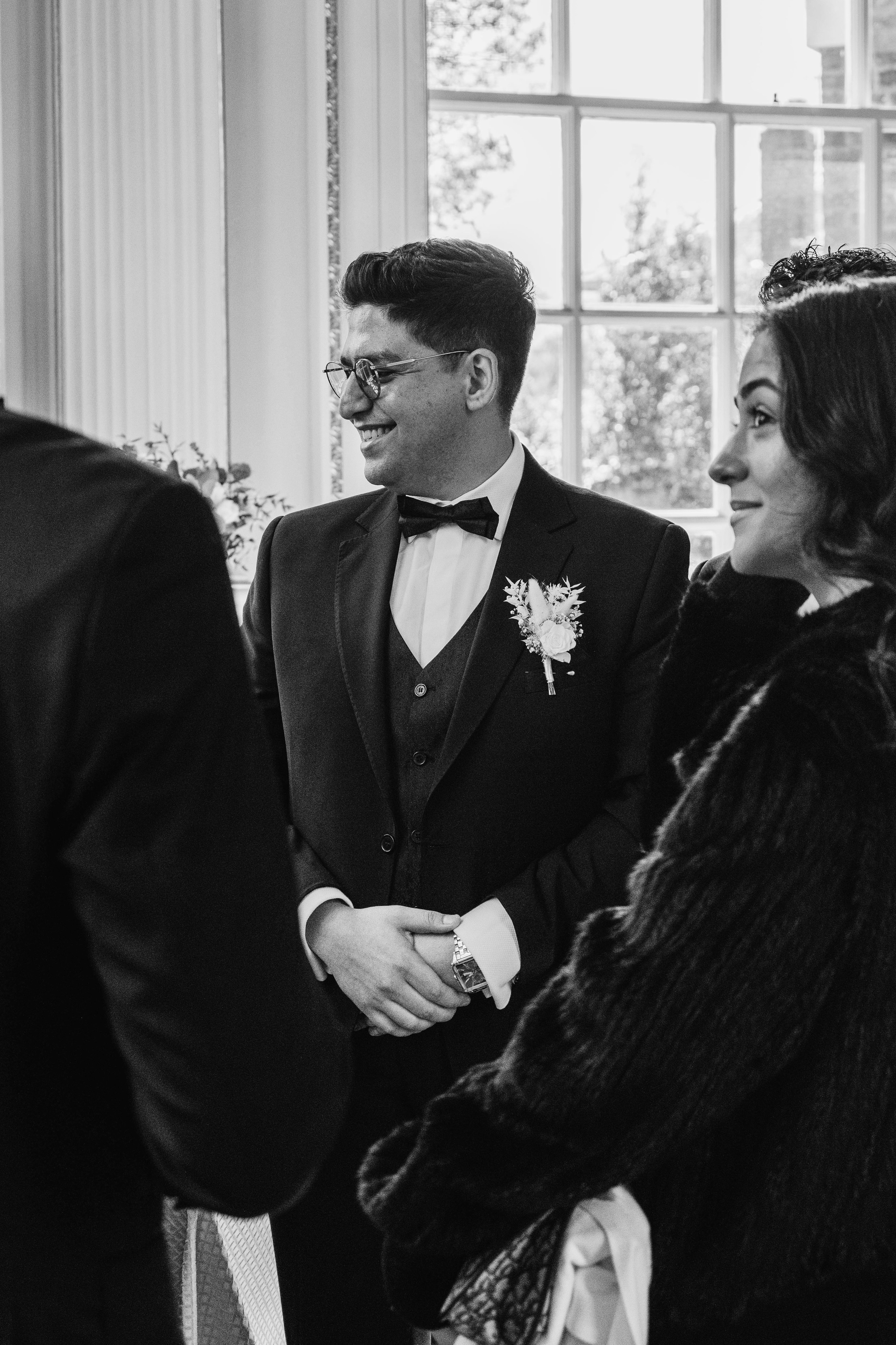 groom in black and white photo smiling with guests
