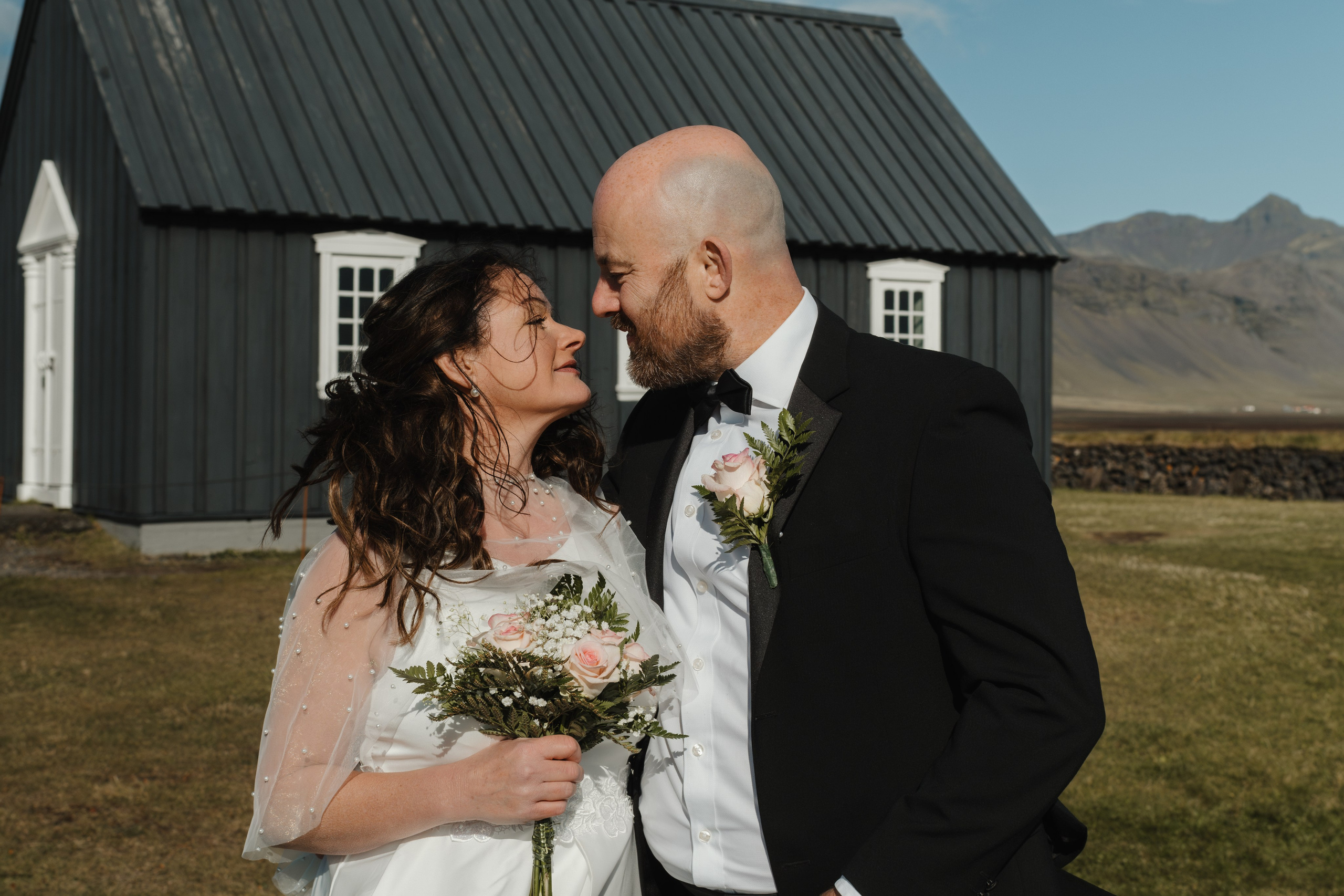 Bride and groom standing in front of the iconic black Búðakirkja, with dramatic Icelandic skies above.