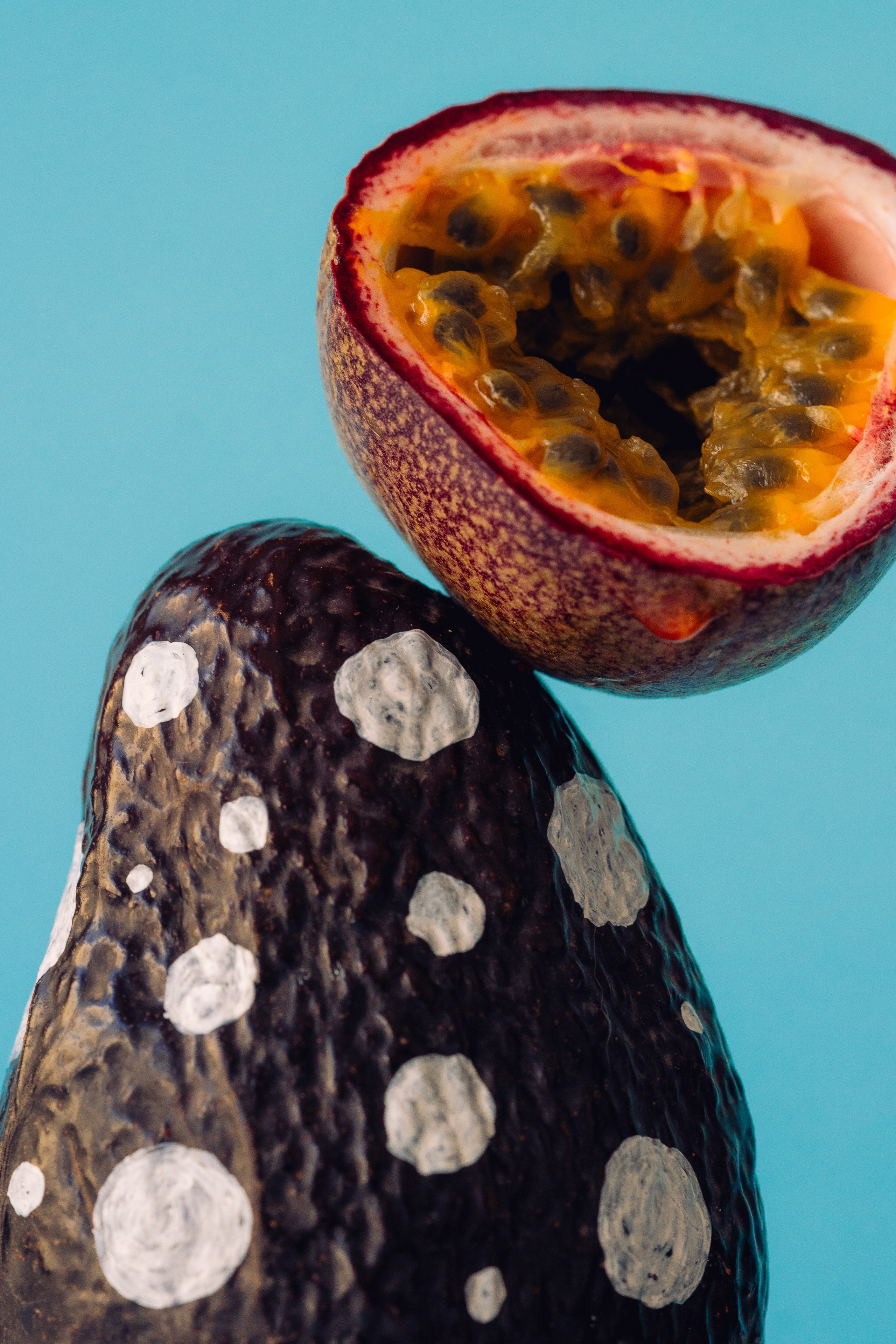 Dotted Design Painted Passion Fruit and Avocado. Creative display of dotted design painted maracuja and avocado on a bright blue backdrop.