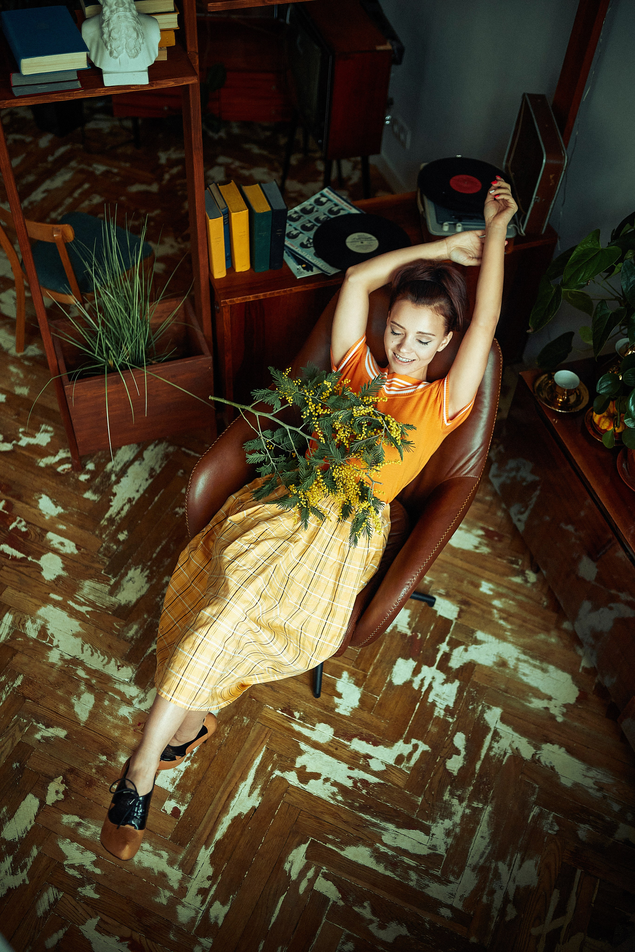 Девушка в юбке и оранжевой футболке сидит в кресле откинувшись назад