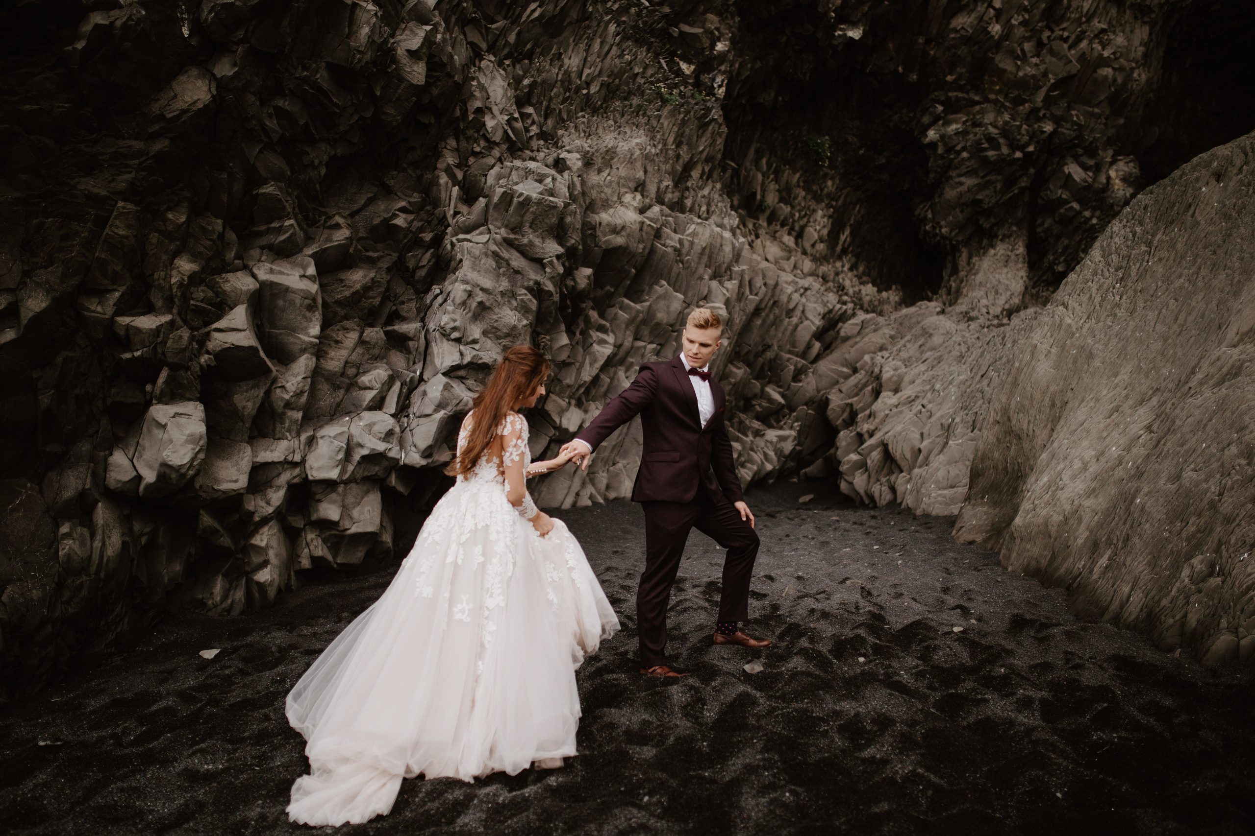 Love and adventure—couple walking along Reynisfjara Beach, Iceland, with the Reynisdrangar sea stacks in the distance.