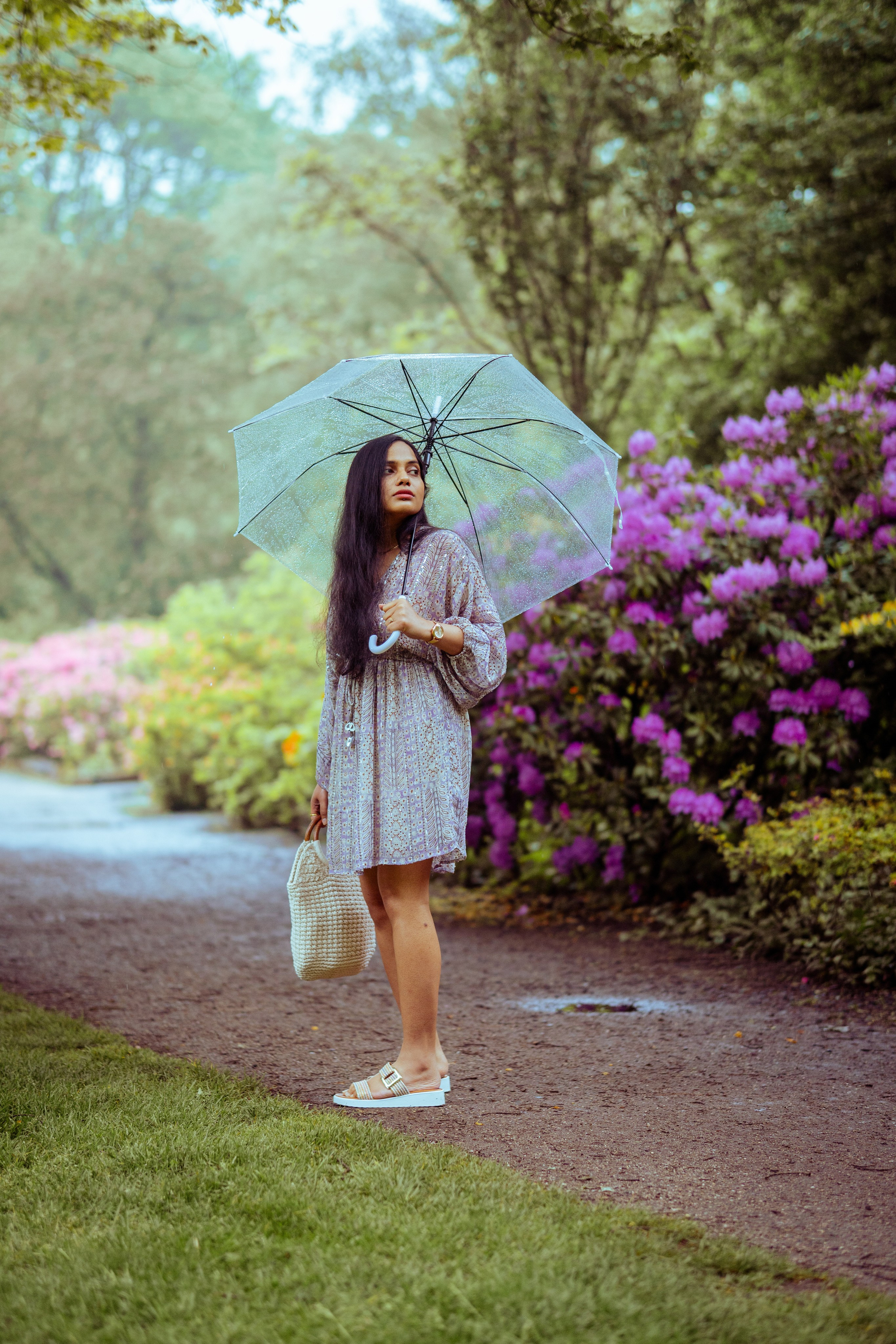 woman standing in a flower park and holding a transparent umbrella 
