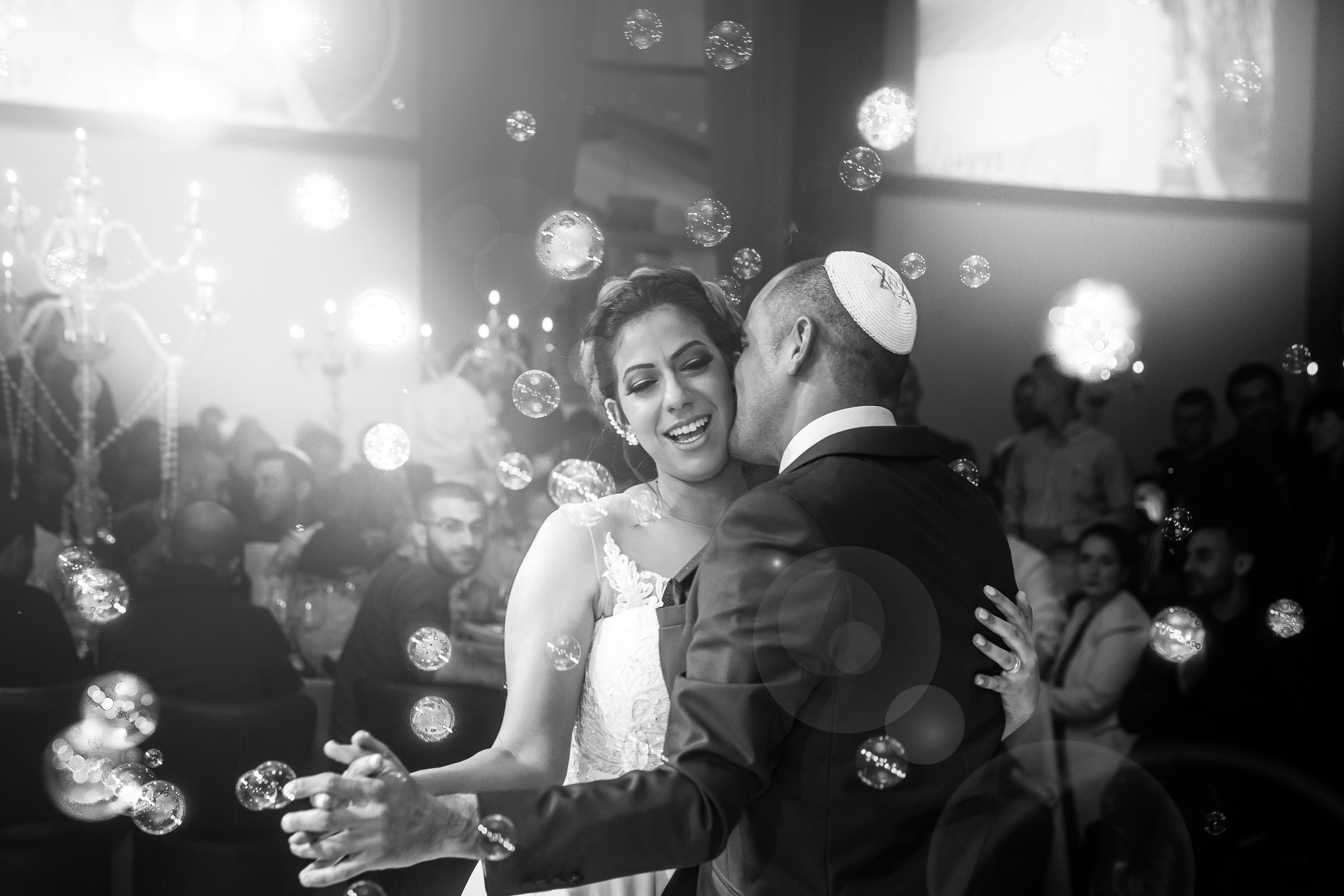Bride and groom sharing an emotional first dance surrounded by floating bubbles and soft light, captured in a candid black-and-white documentary wedding photograph in Israel