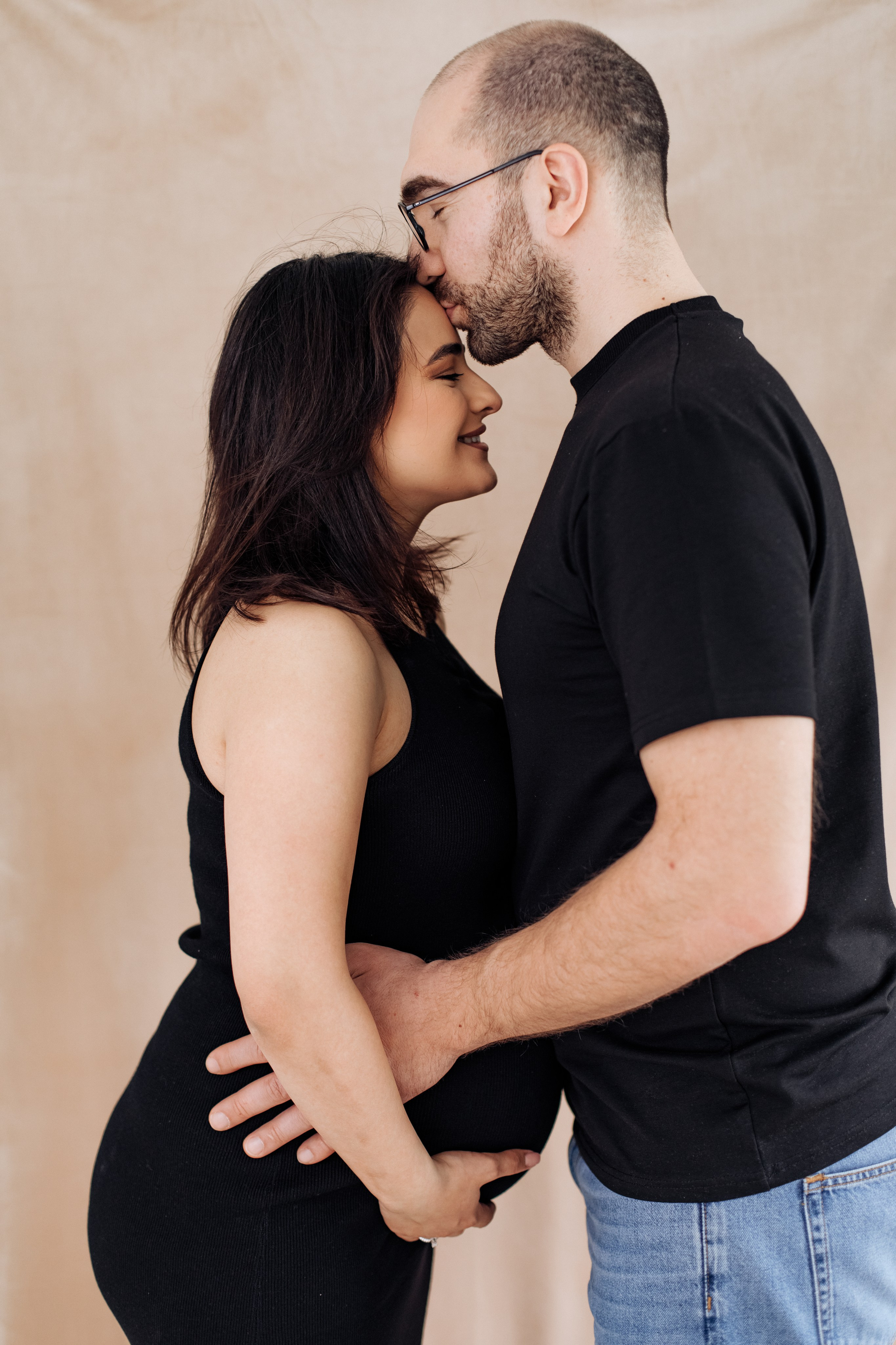 Mann umarmt seine schwangere Frau und küsst sie liebevoll auf die Stirn.