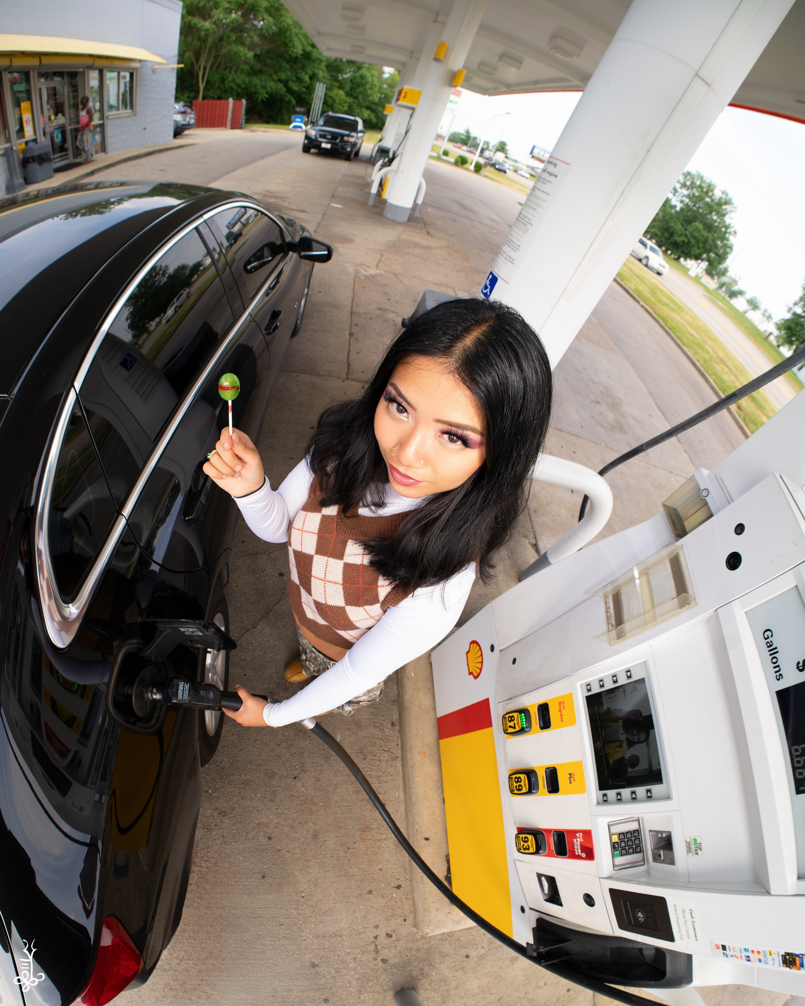 Model in white top and camo pants stepping out of a black car at gas station