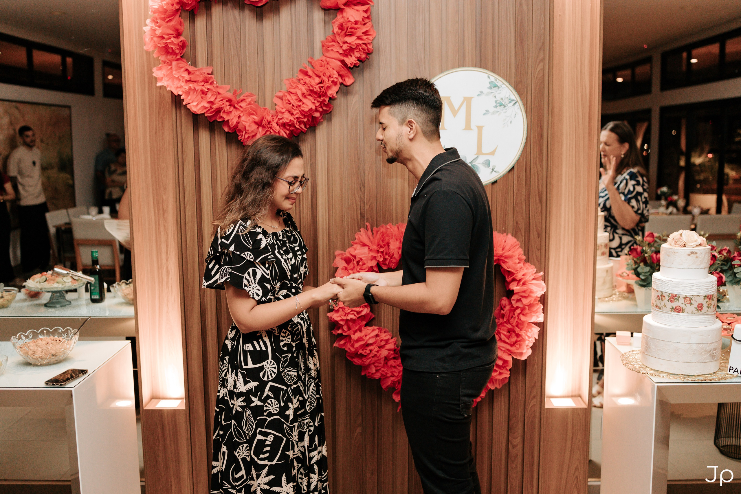 Casal sorrindo diante de corações vermelhos na parede.