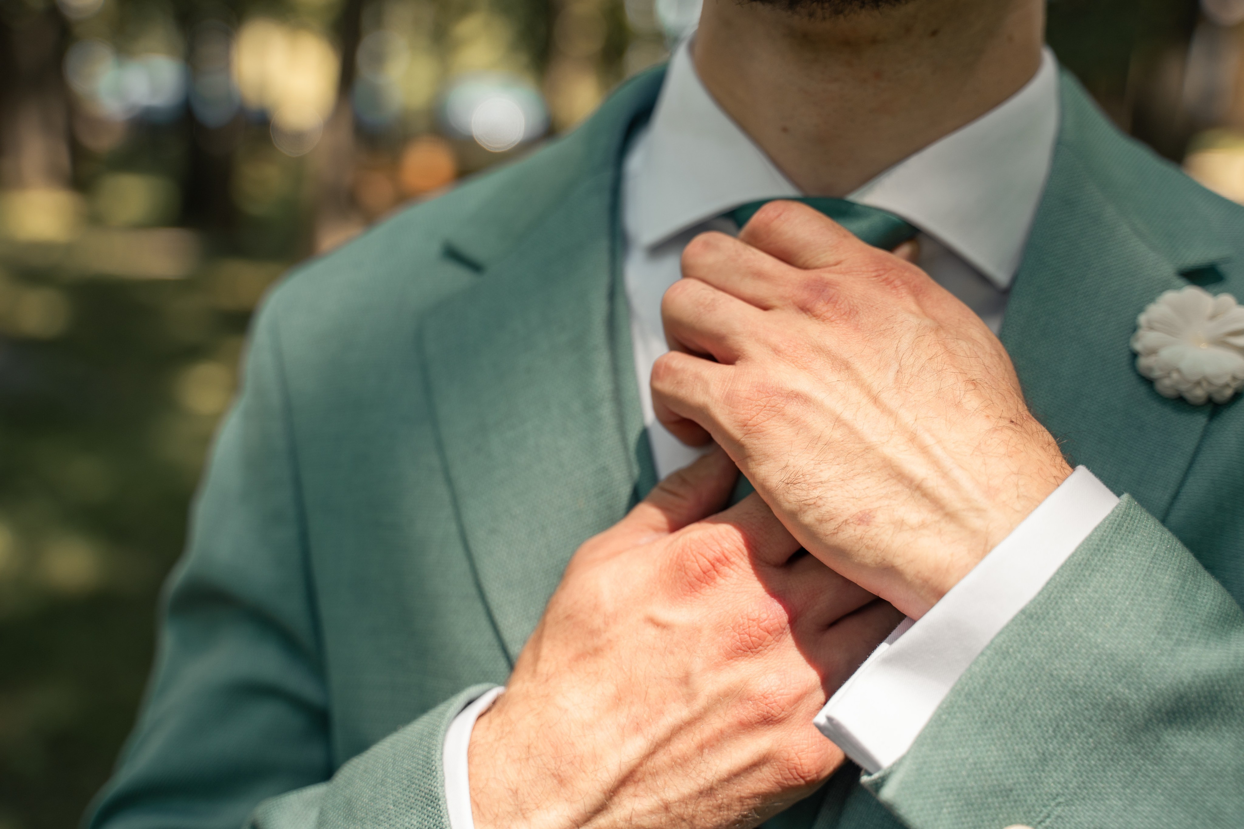Detaliu mire ajustându-și cravata verde, costum de nuntă elegant în aer liber, pregătiri mire București, fotografie macro detalii nuntă, incadru.ro.