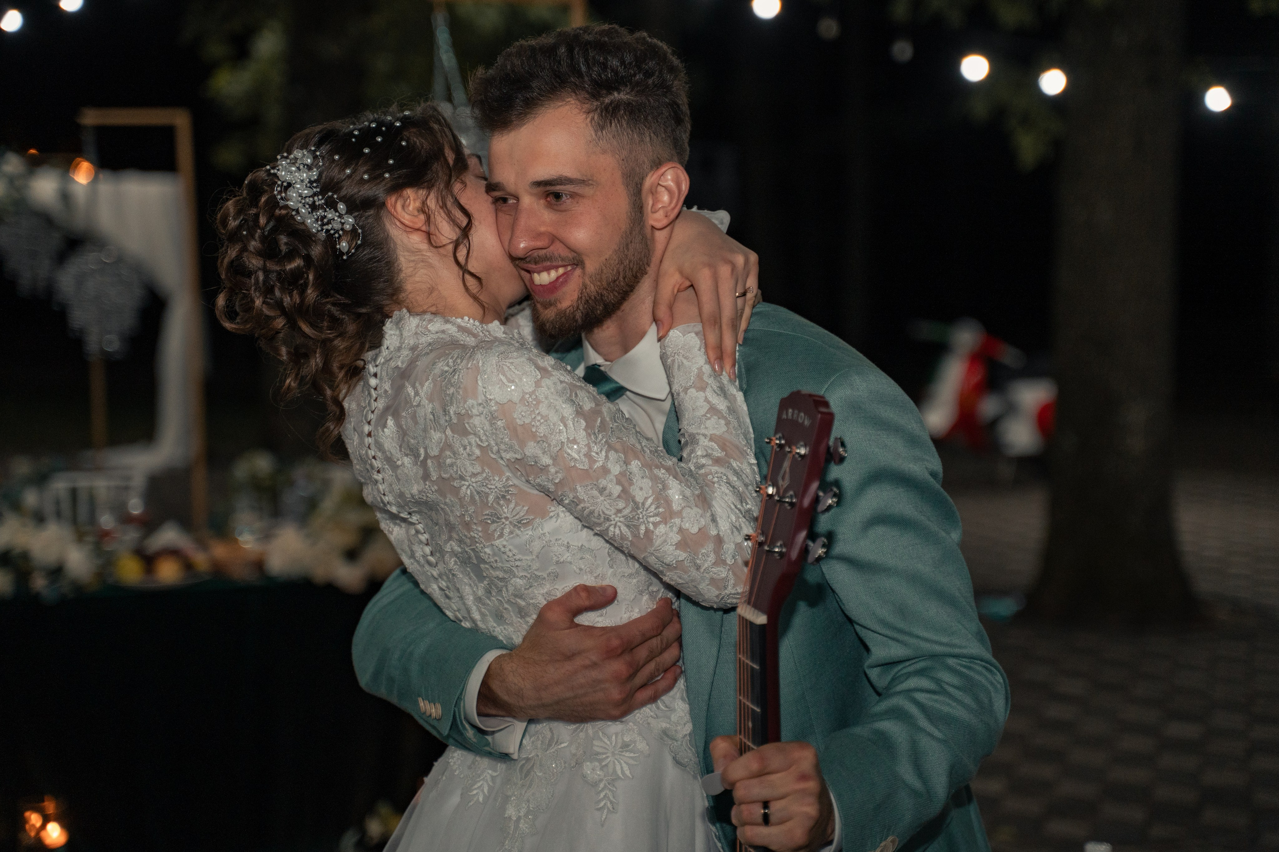 Mireasă îmbrățișând mirele care ține o chitară, fundal cu luminițe tip ghirlandă, nuntă de noapte, incadru.ro.