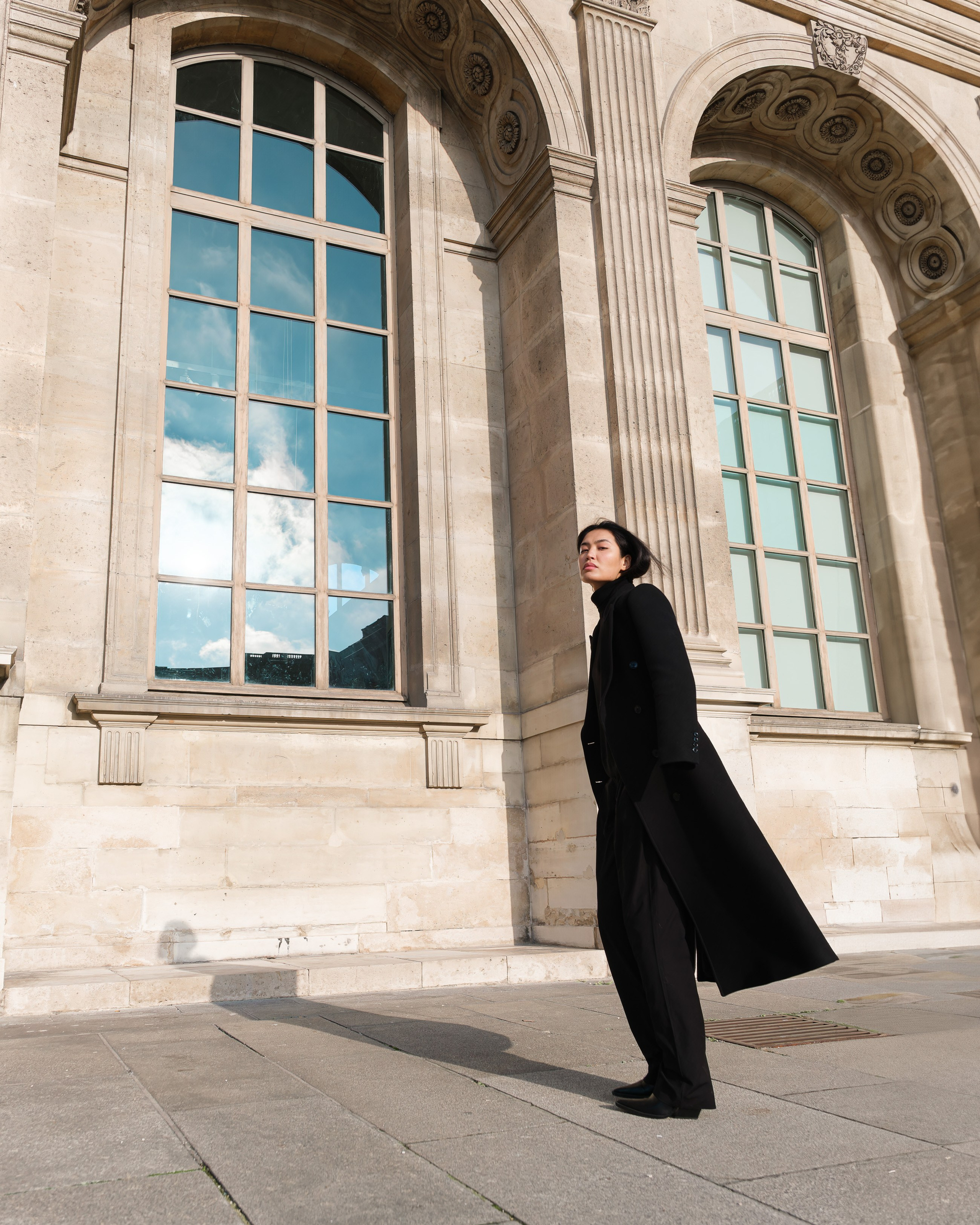 Editorial fashion campaign featuring a black wool coat next to classical Parisian architecture
