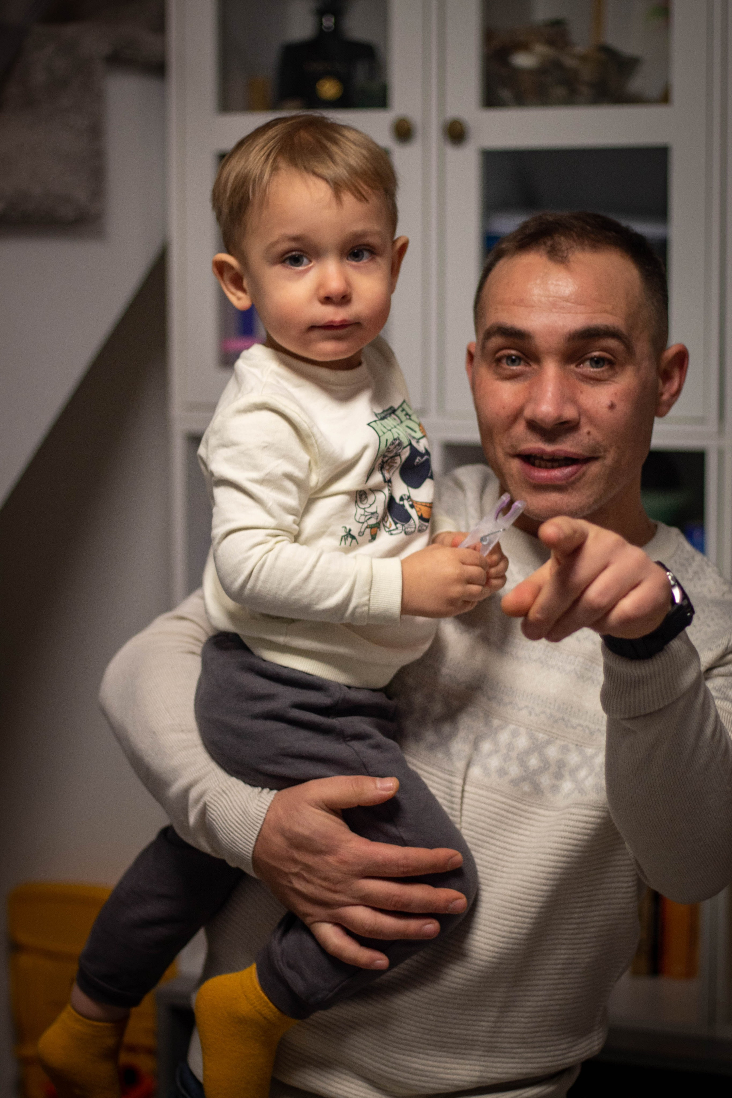 Young child hold by his father and smiling indoors with natural light.