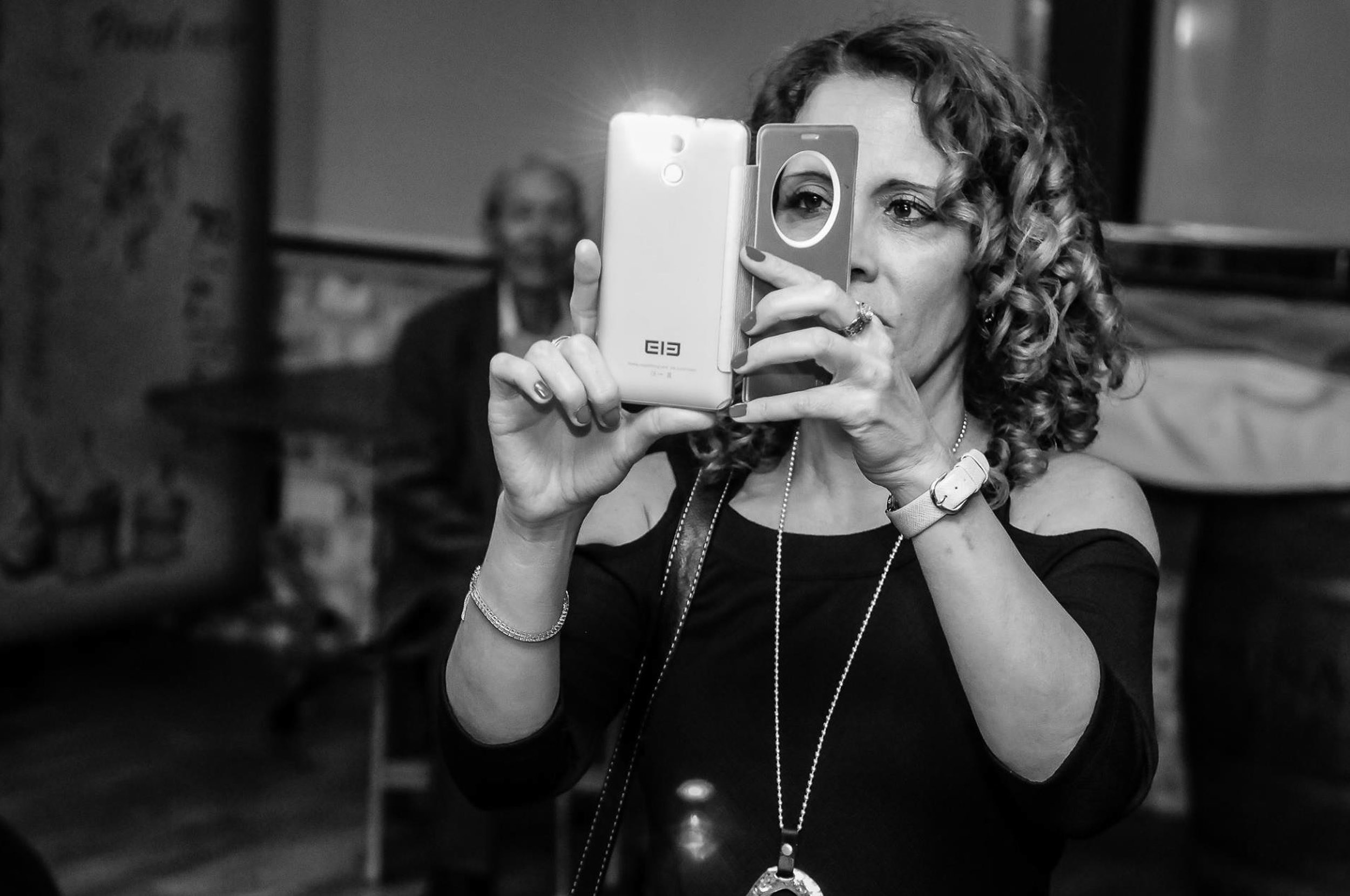 Candid black and white wedding photography of a guest taking a picture with a smartphone in Israel