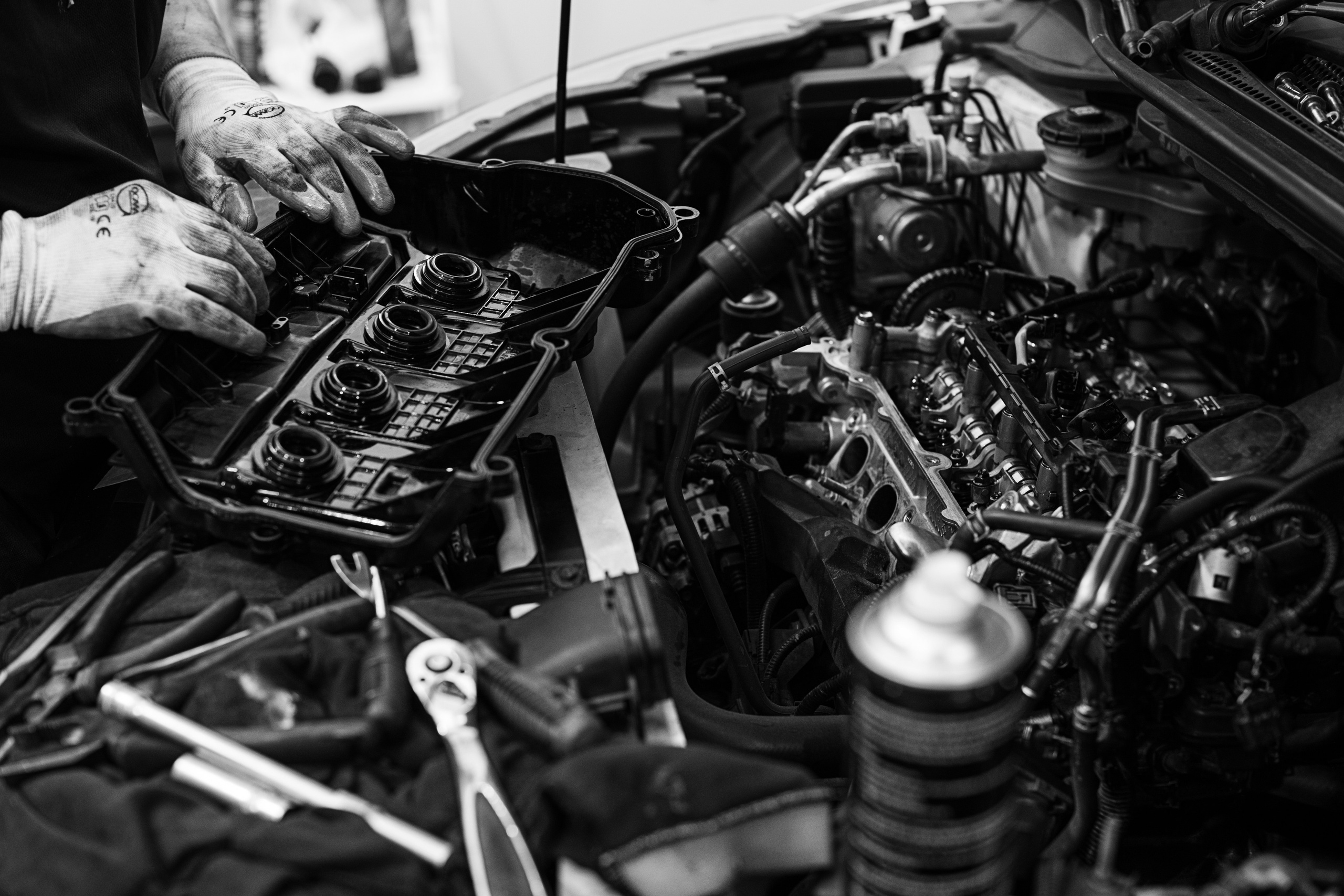 Close-up black-and-white photograph of a mechanic’s gloved hands working on the engine of a classic car at The Garage by Classic Motorworks in Singapore. Captured by Mirrorklezz Photography, this image emphasizes the intricate process of vintage car restoration, showcasing tools, engine components, and the detailed craftsmanship involved in maintaining automotive heritage. https://www.classicmotorworks.com.sg/