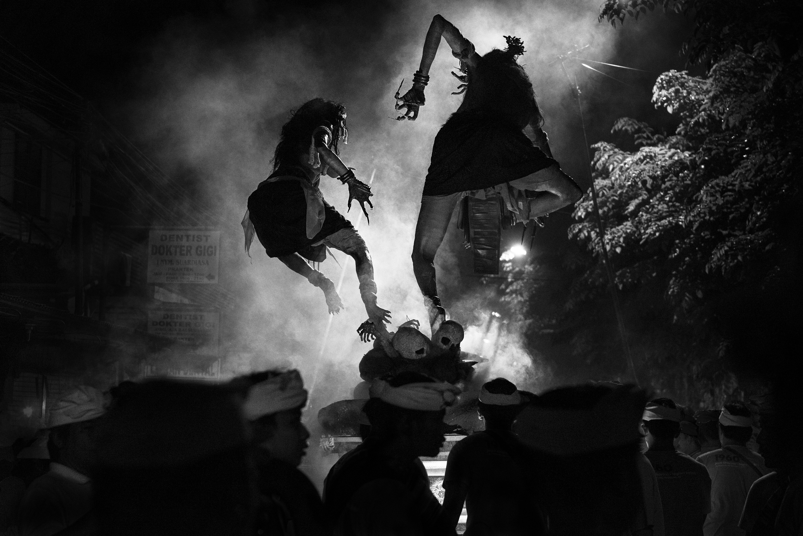 A dramatic black-and-white photograph capturing two figures leaping in mid-air during a traditional cultural performance, surrounded by smoke and dim lighting. The silhouettes and dynamic movement create a sense of mystery and energy, evoking the rich storytelling of the event. This image showcases the photographer’s expertise in capturing cultural performances and dynamic scenes, ideal for clients seeking impactful visual documentation for editorial, event, or cultural projects.
