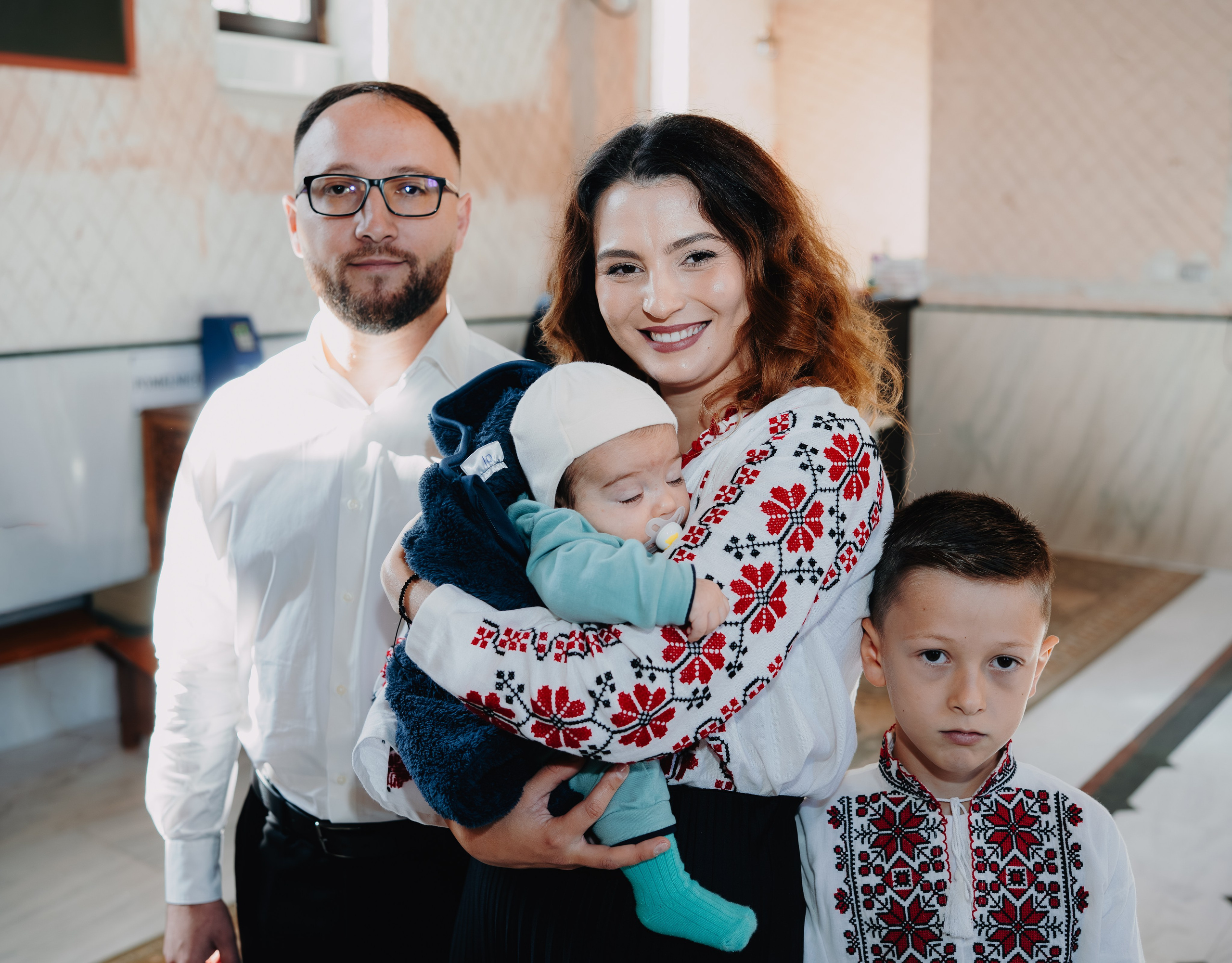Grupul familial așteaptă solemn începerea slujbei de botez a lui Arthur Mihail în Catedrala din Bârlad. Nașa, nașul (fiul ei) și mama pruncului stau alături, privind cu liniște și anticipare.