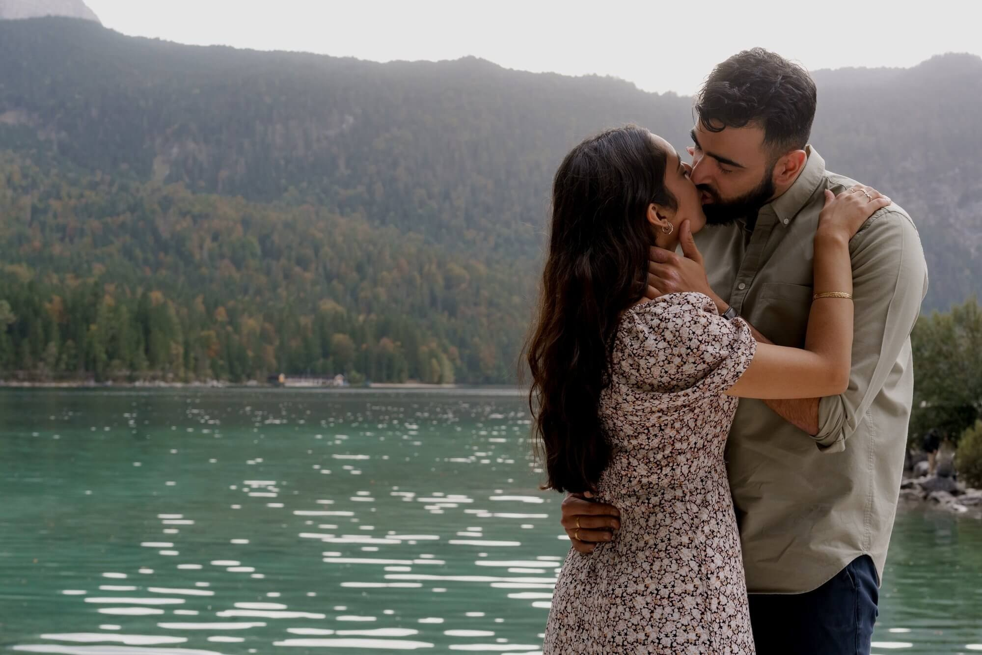 Couple embracing in a close portrait with Eibsee and mountain forest in background during engagement session