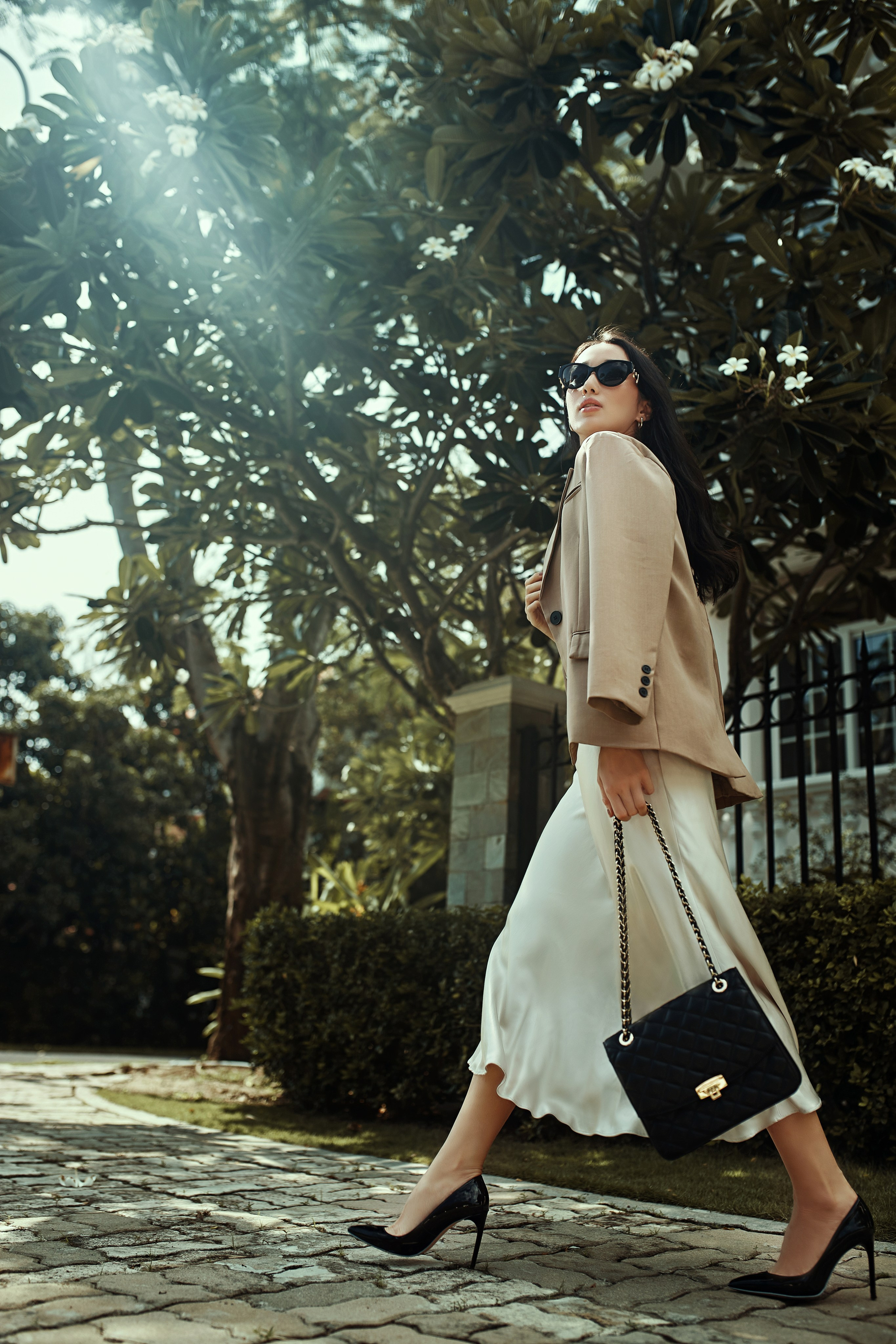 Стильная девушка с сумкой идёт по улице в солнечную погоду