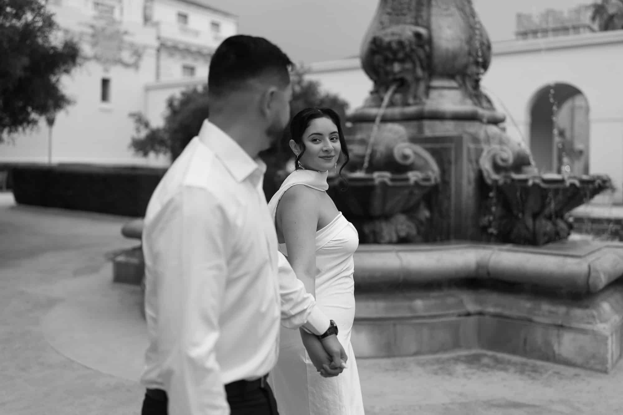 Bride and groom holding hands, walking near fountain at Pasadena City Hall (black and white)