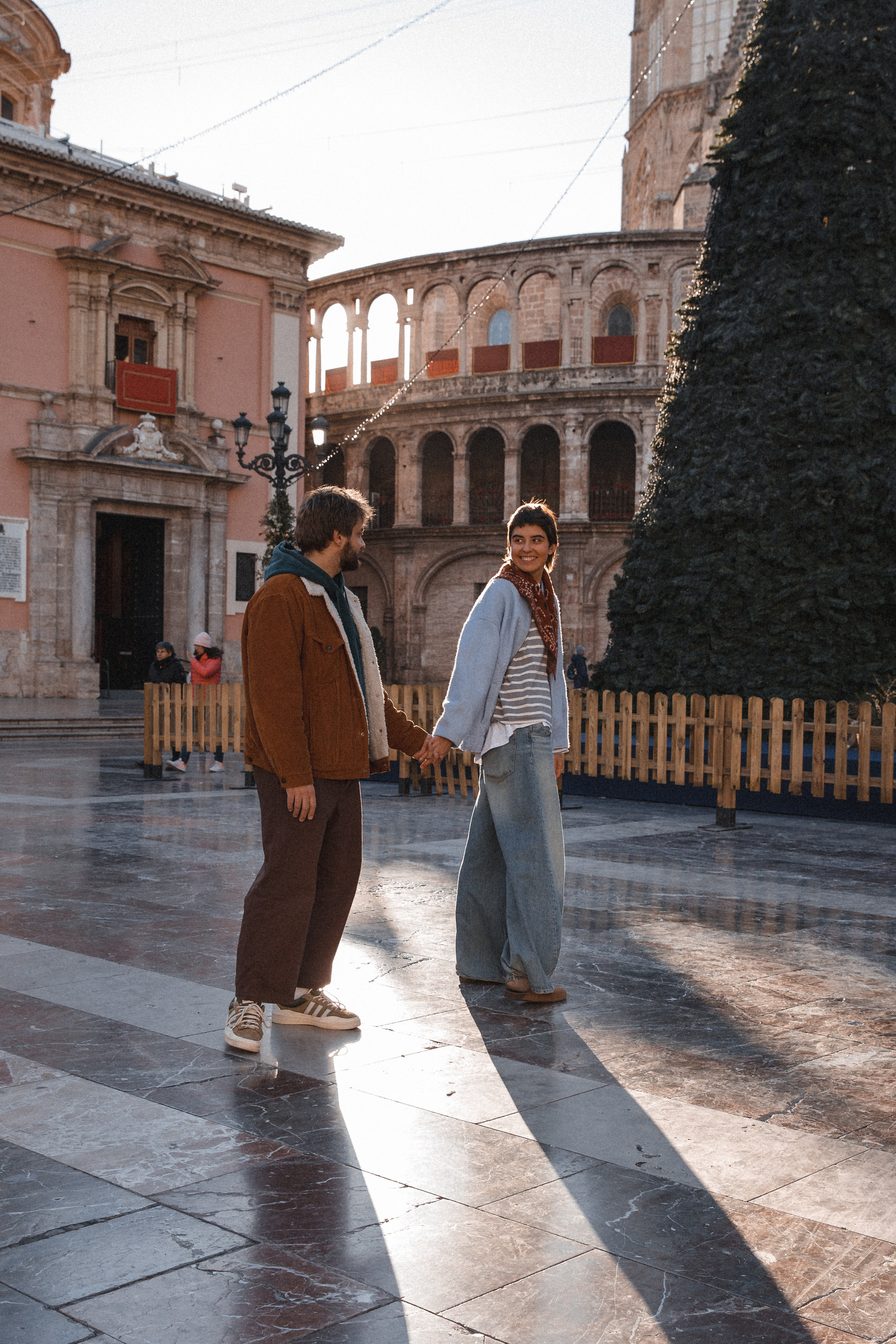 Tender black and white portrait of a couple sharing an affectionate moment in front of the ancient stone façade of Valencia Cathedral, capturing the essence of love and history in Valencia, Spain.