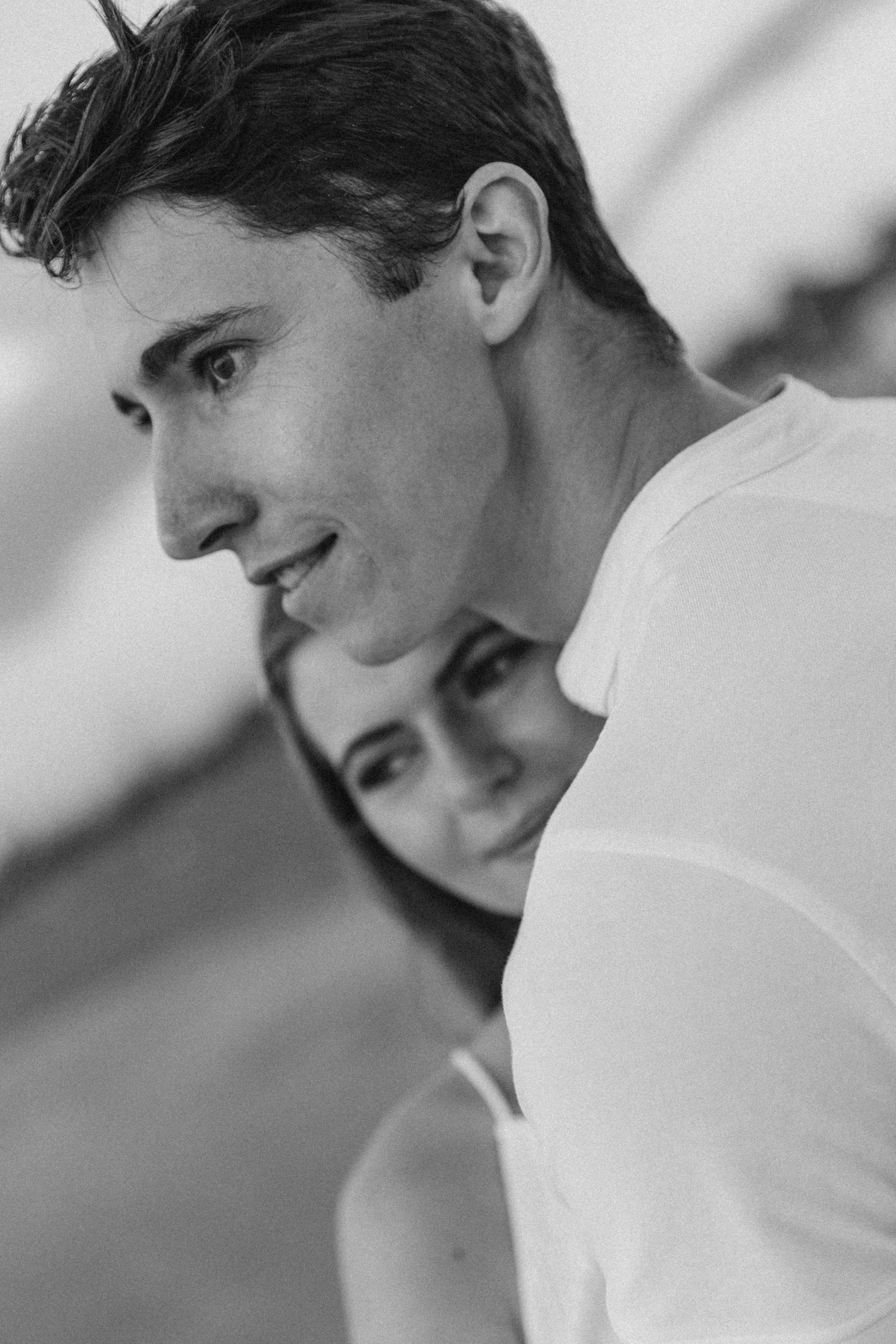 Black and white close-up of a couple embracing, with the man gazing ahead and the woman softly smiling beside him, capturing a quiet moment of connection on the beach in Valencia, Spain.